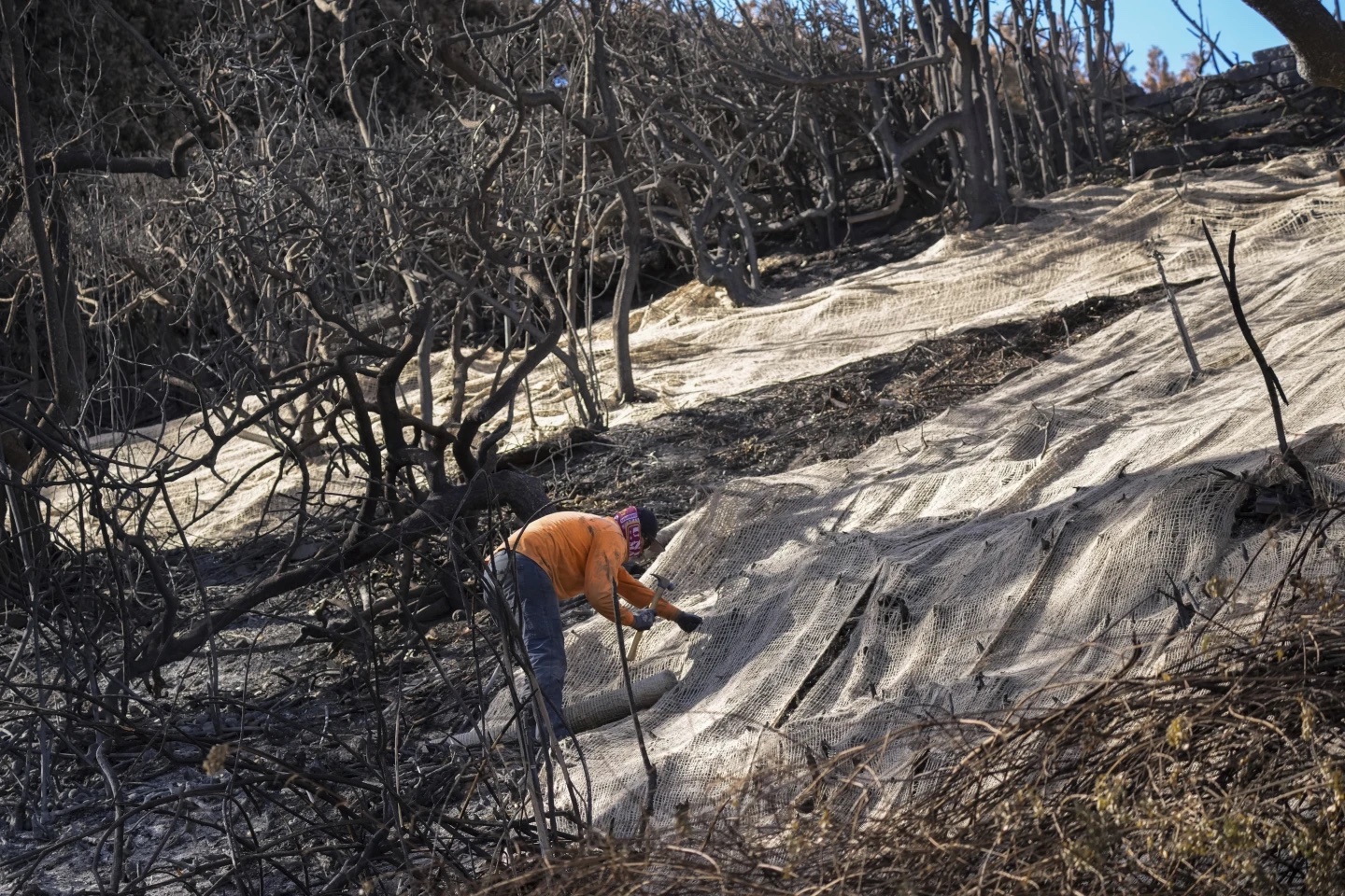 A worker secures netting on a hillside.