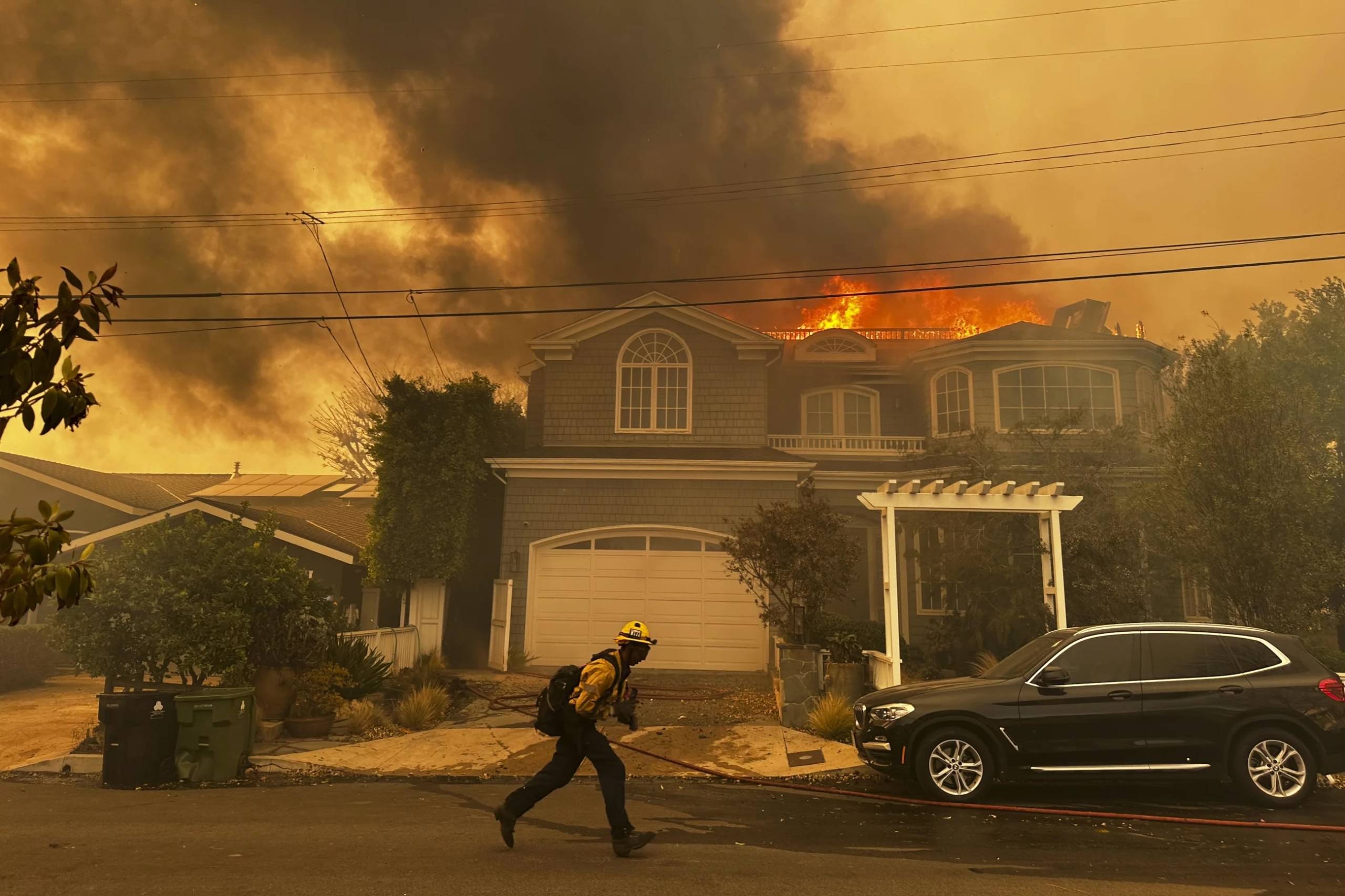 A firefighter passes a house with its roof on fire in a suburban street.