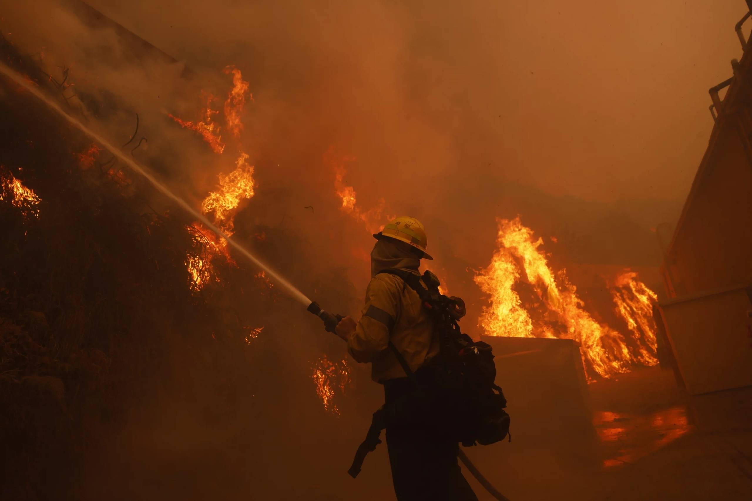 Firefighter points hose at flames, surrounded by orange glowing smoke.