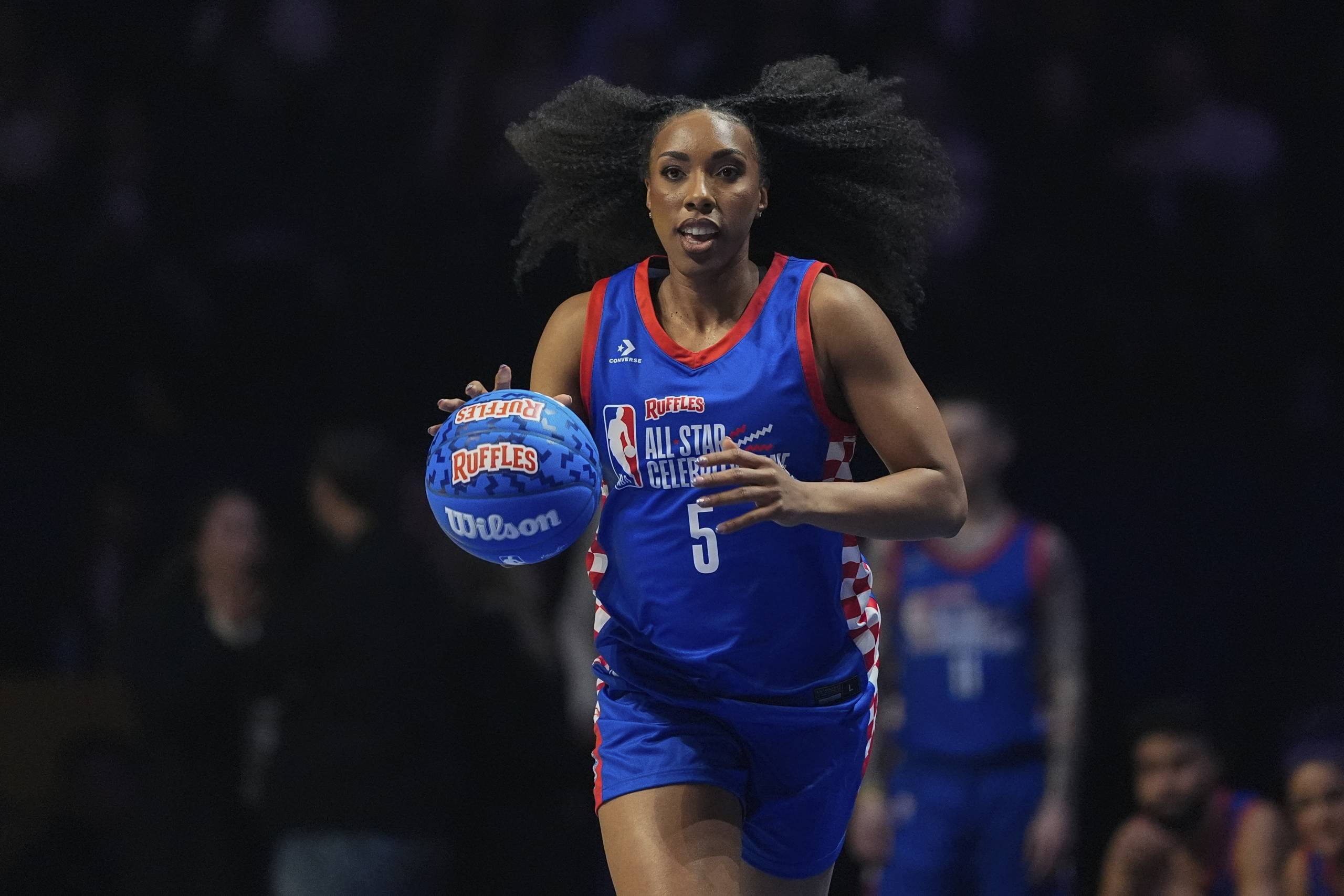 A woman in a blue jersey dribbles a basketball.