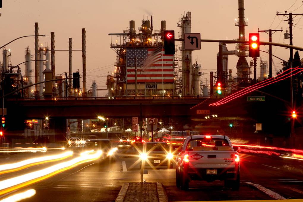 A view of traffic with an oil refinery in the background.