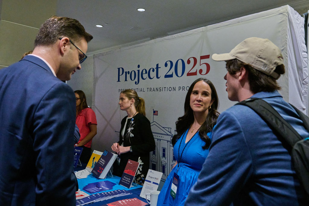 A group of people stand behind a table with a 'Project 2025' banner behind them.