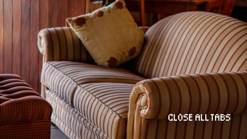 Striped sofa with a floral pillow next to a patterned ottoman in a wood-paneled room. Text reading "CLOSE ALL TABS" in the corner.