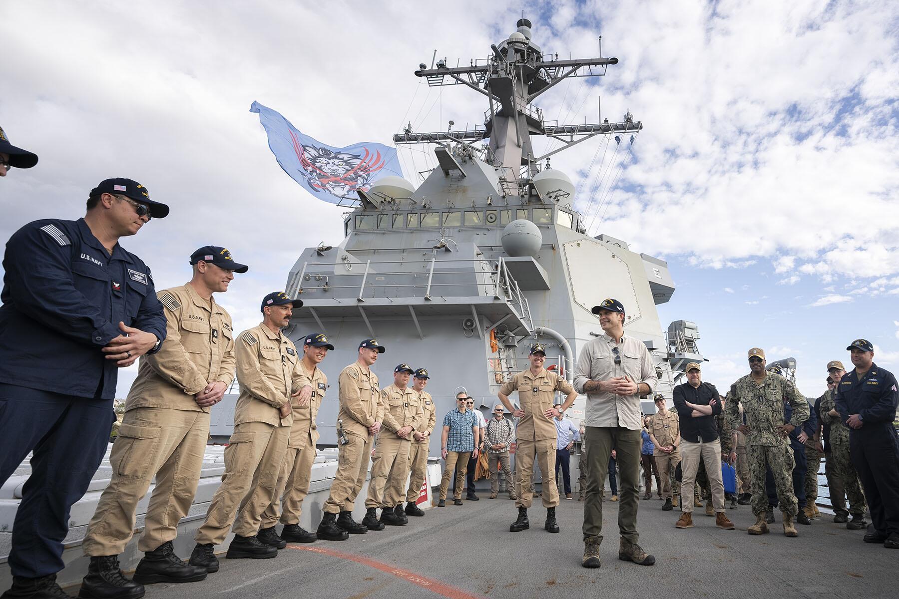 People standing in front of a large ship with clouds in the background.