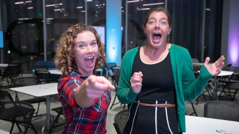 Two women show surprise at something behind the camera.