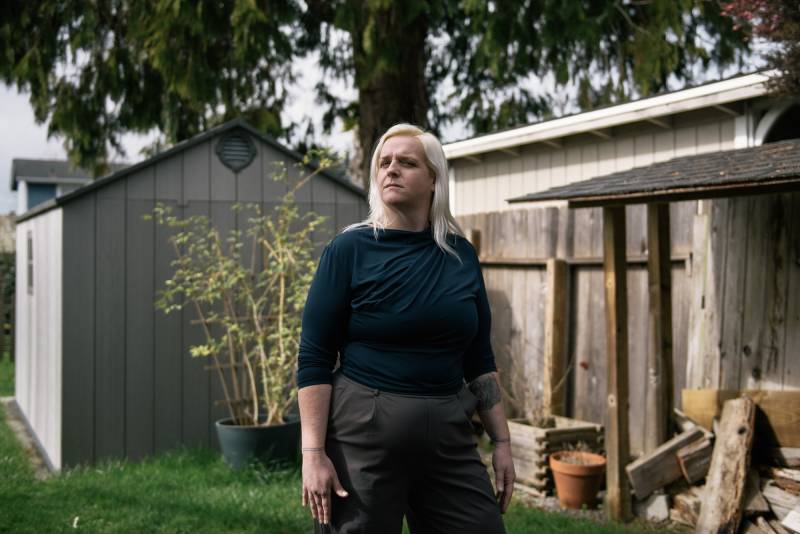 A white woman wearing a green shirt stands outside in a backyard.