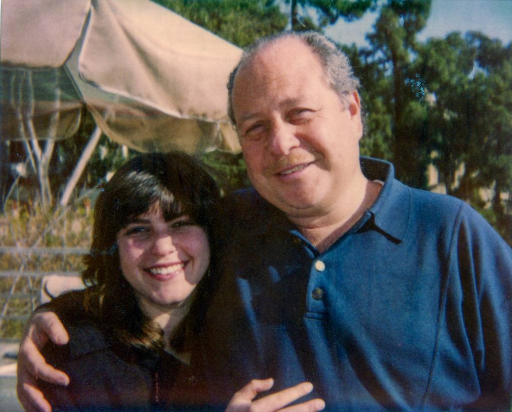 A middle-aged man smiles at the camera with his arm draped around a smiling young woman, his daughter.