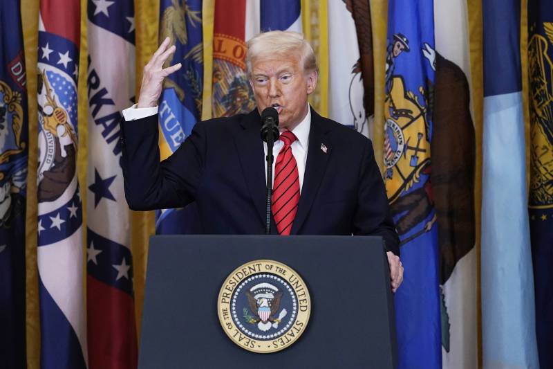 Trump stands in front of a podium with his hand up.