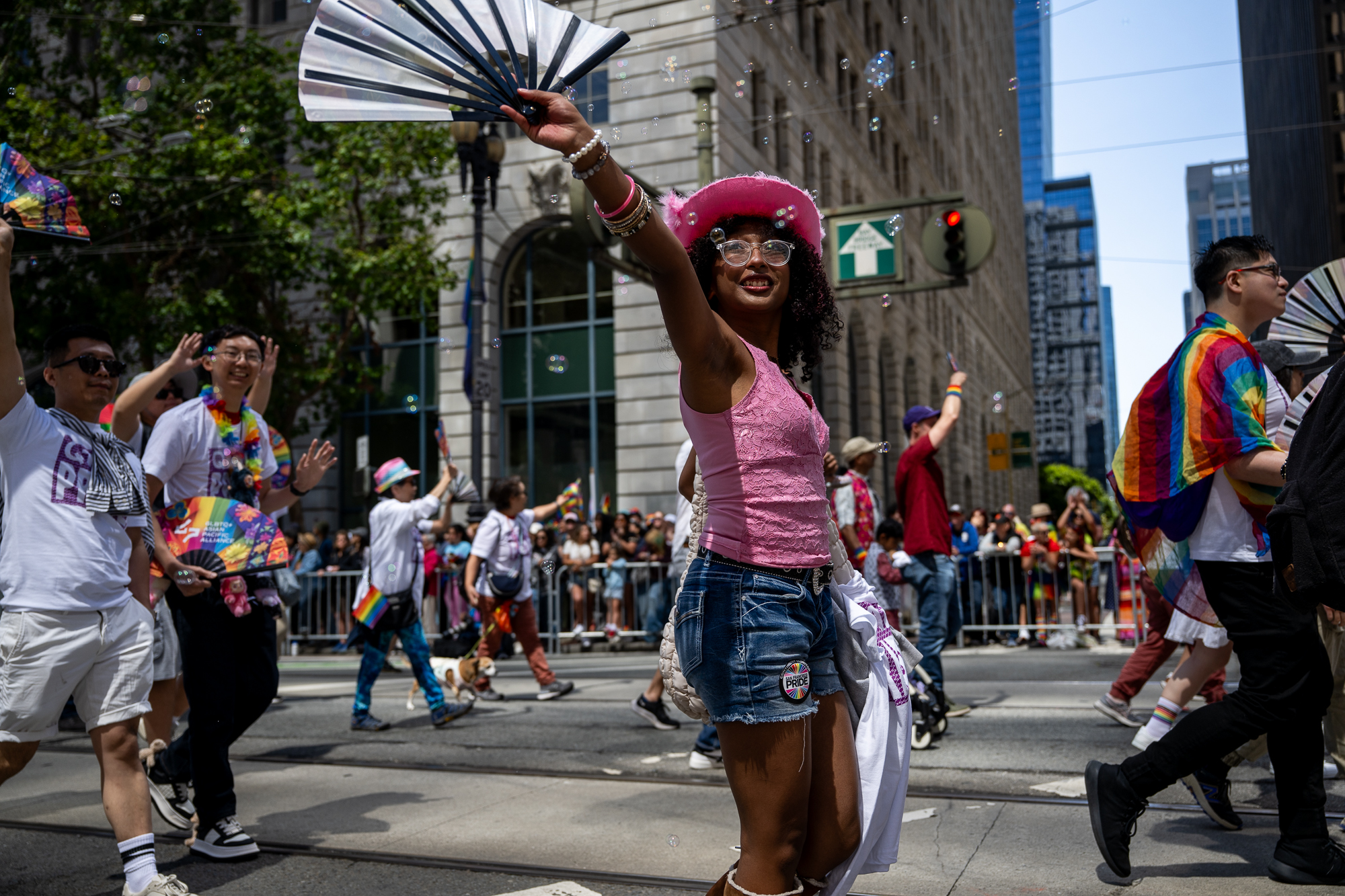 Uma pessoa vestindo uma blusa rosa e segurando um ventilador branco acima da cabeça na rua entre várias pessoas.
