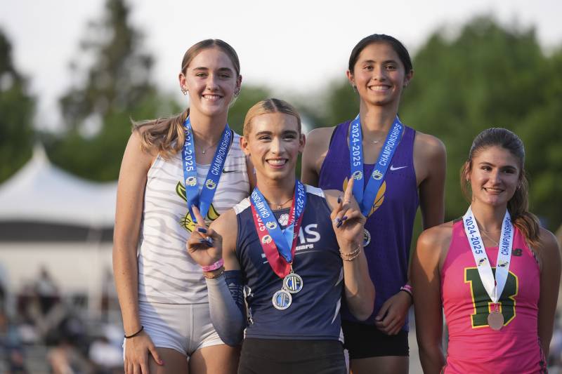 Three young people wearing track and field attire and medals around their necks pose for a photo.