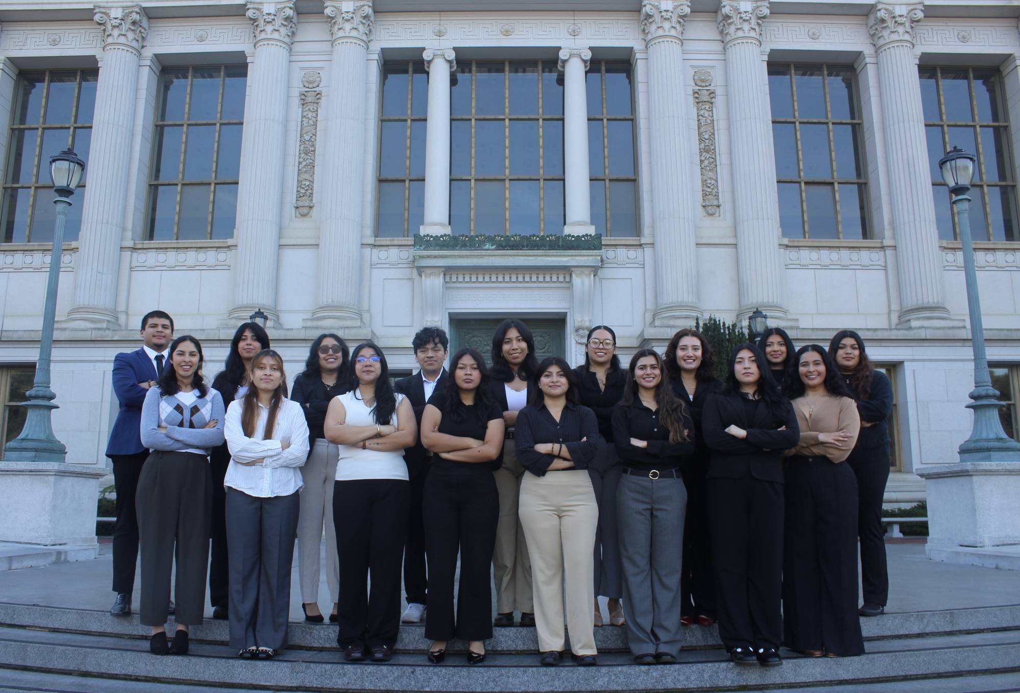 Students from UC Berkeley in professional attire pose with their arms crossed in front of library with big white columns.