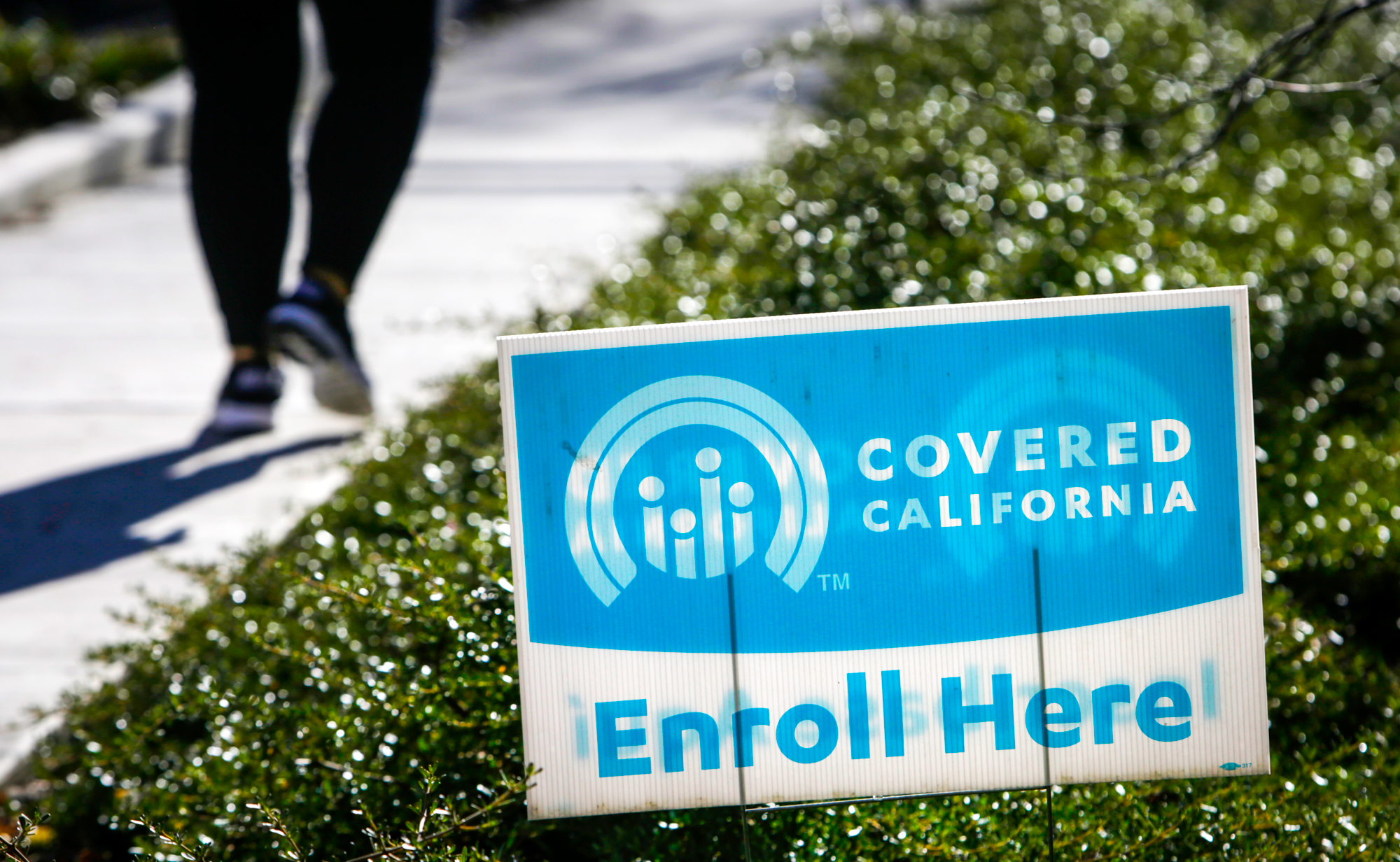 Una persona camina sobre la acera, a lado del patio de una casa donde está el letrero de Covered California.
