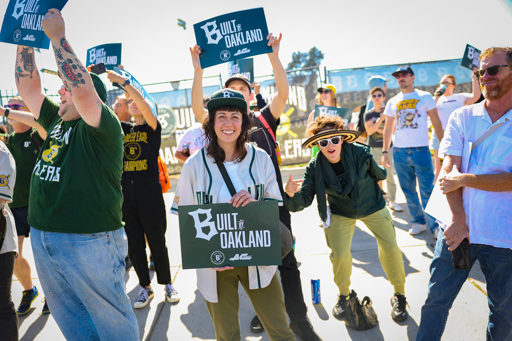 Several people hold green signs that say "Built by Oakland" and cheer.