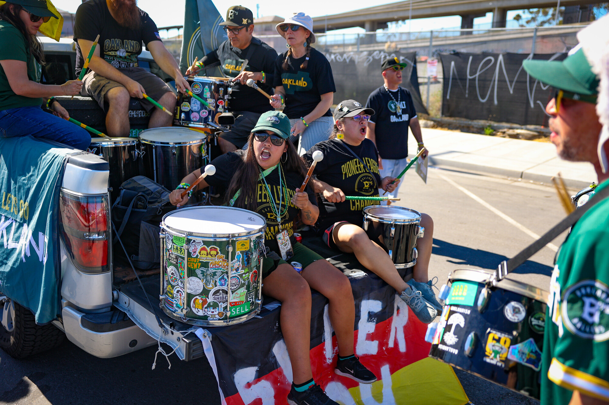 Several people dressed in green clothing are seated in the back of a pickup truck with drums.