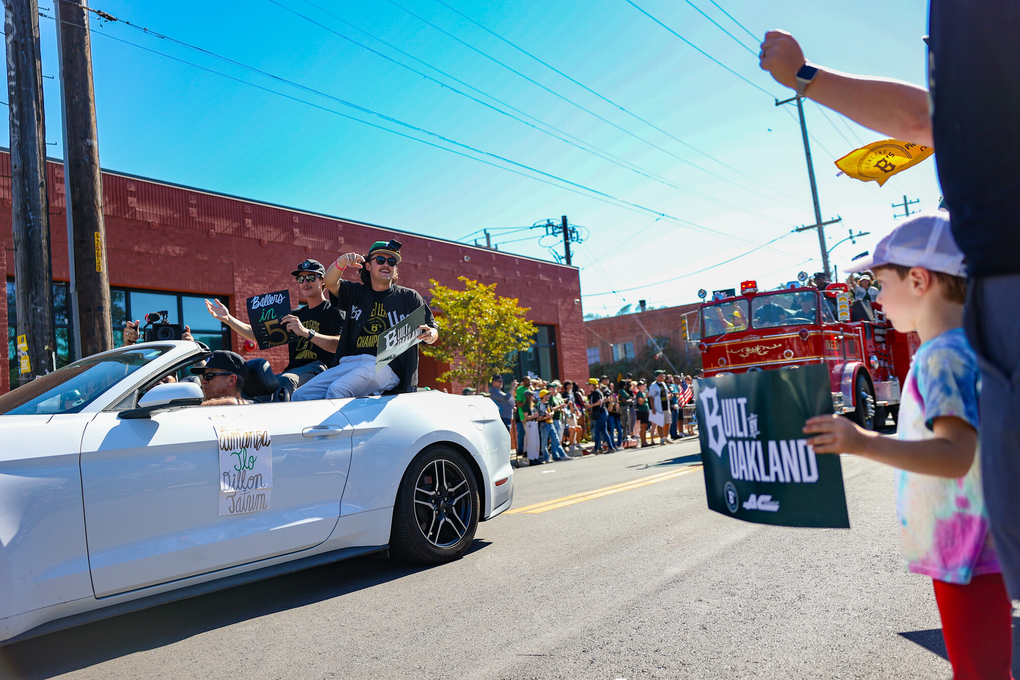 People on both sides of the street wave to people in a white car.