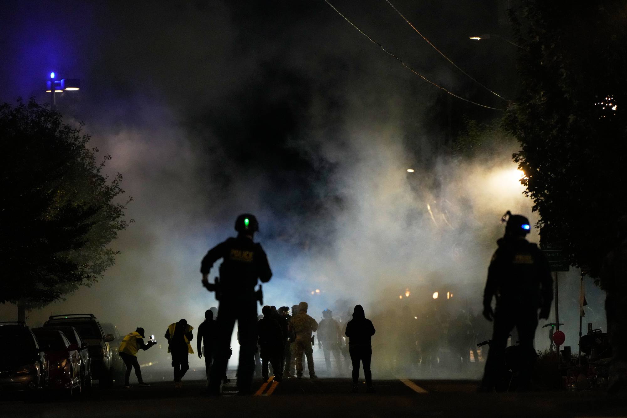 A nighttime photo of several people walking and running in the street with tear gas in the air.