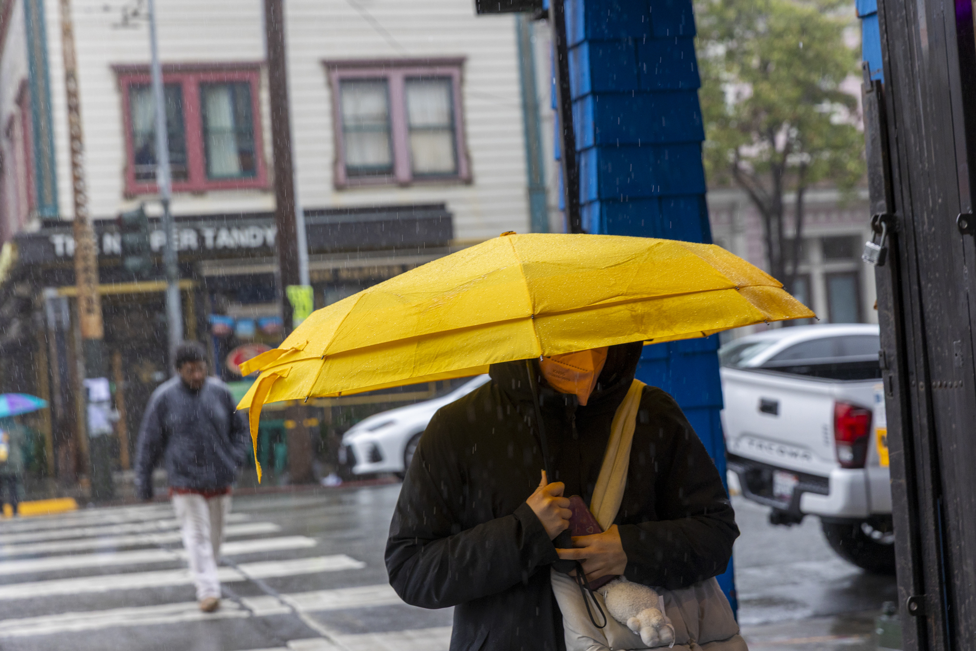A person walks down the street towards the camera. Their umbrella covers their face.