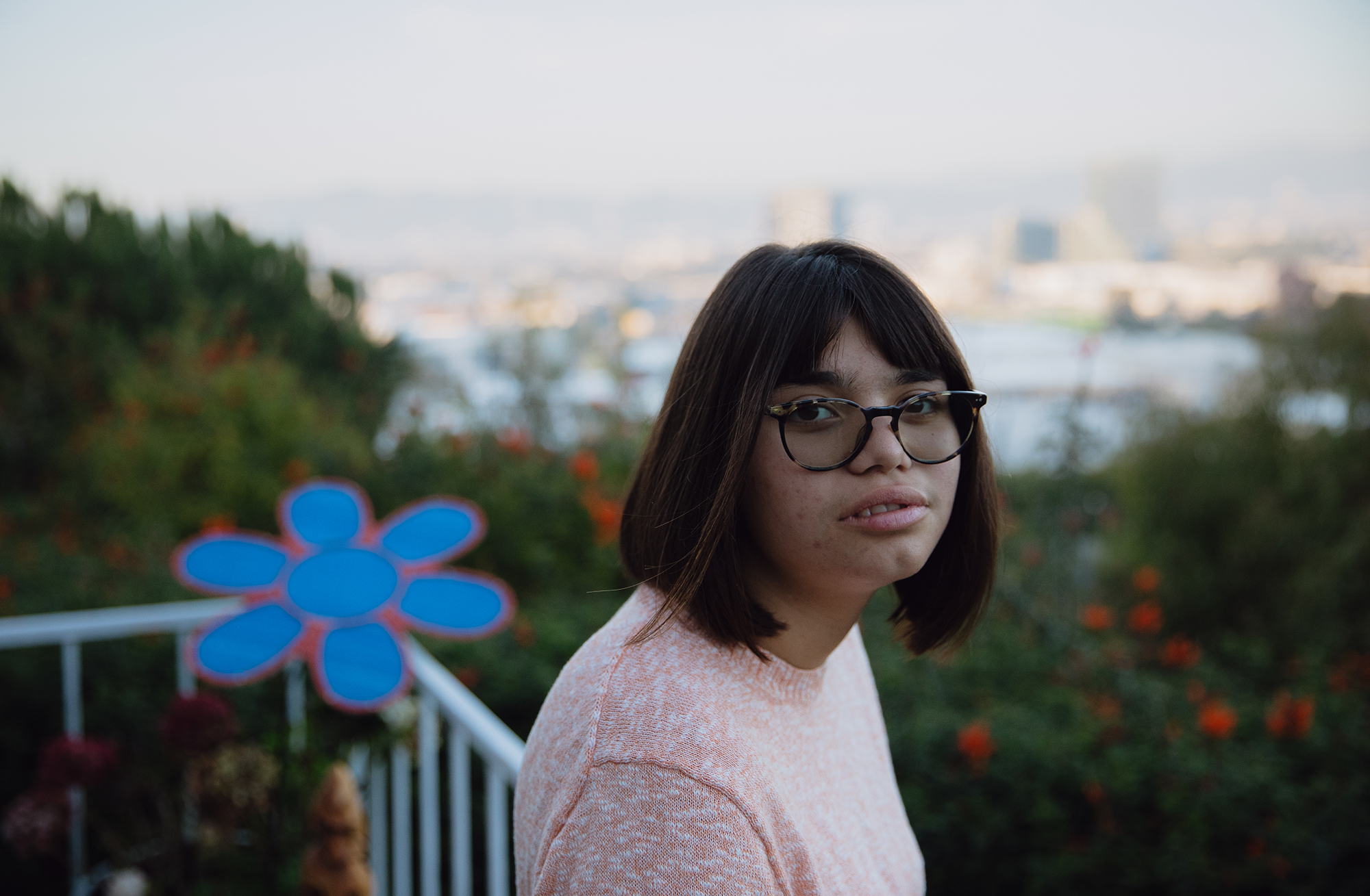 A young woman with glasses and a pink shirt stands outside on a deck.