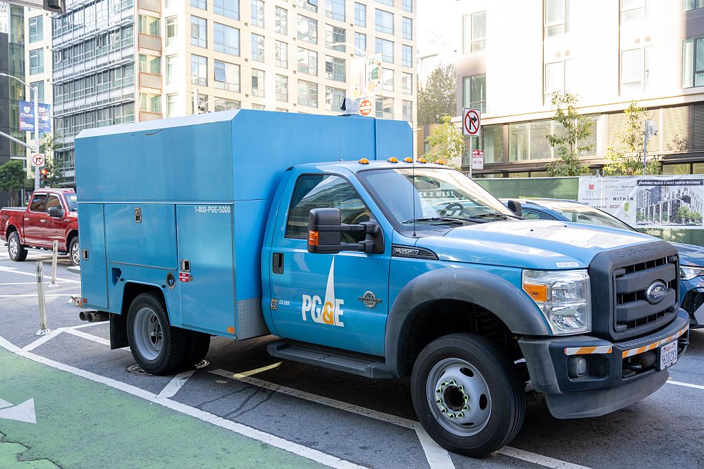 A blue truck with 'pg and e' logo on it is parked on a city street.