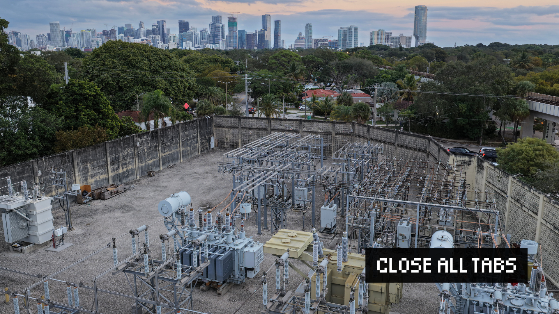 An aerial view shows high voltage power lines running through a sub-station along the electrical power grid. Green trees and the Miami skyline appear in the background. The words “CLOSE ALL TABS” appear in pixelated text in the lower right with a black background.