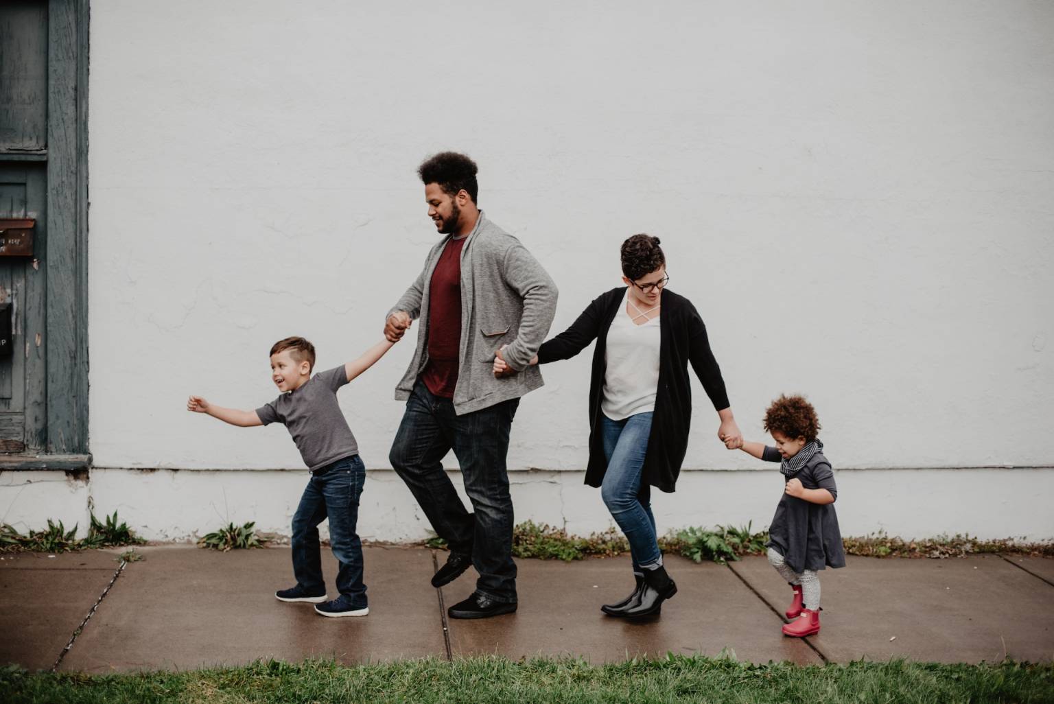 Familia de cuatro personas saltando por una calle mojada, tomados de la mano.