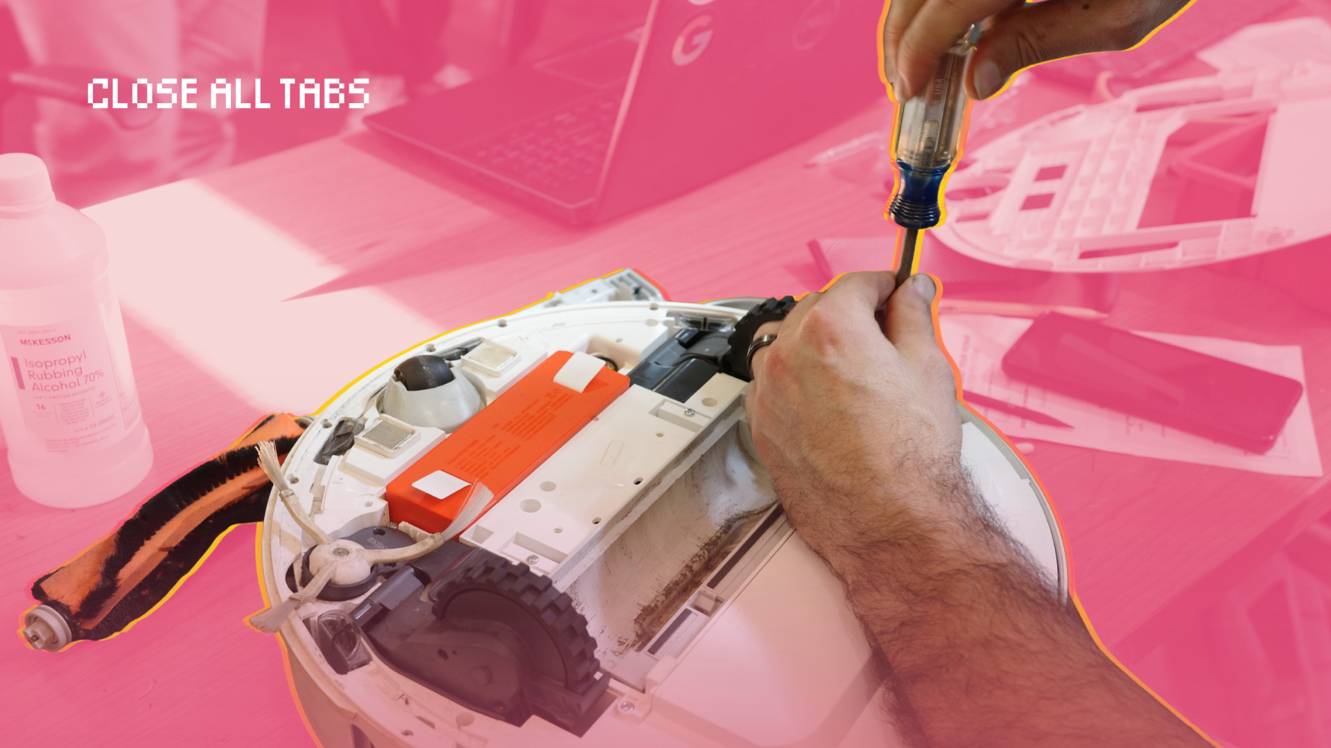 Close-up of a volunteer using a screwdriver to repair the underside of a robot vacuum, its internal components exposed on a worktable, with tools and parts scattered nearby. The image has a pink overlay with “Close All Tabs” in the top left.