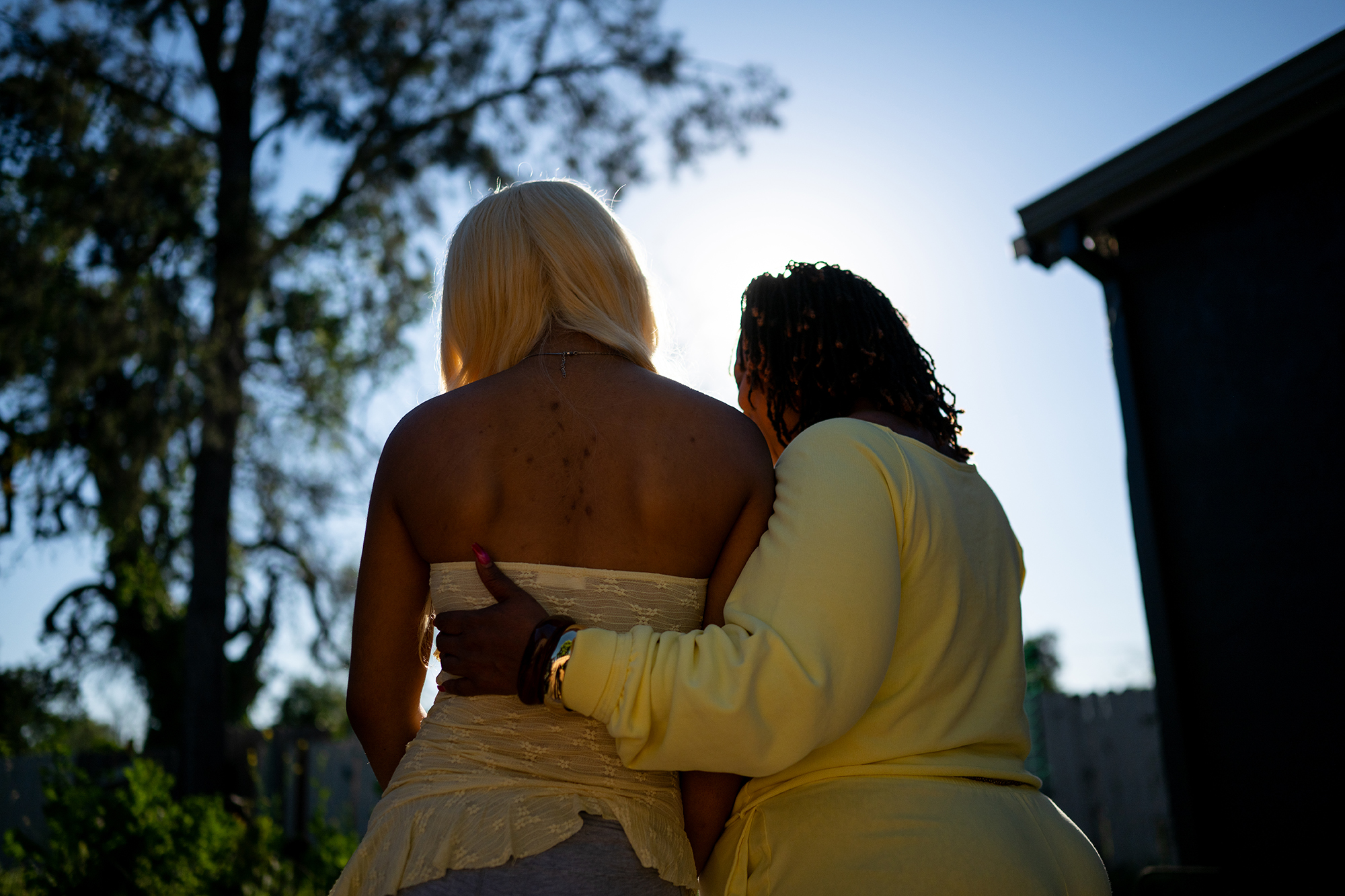 A 17-year-old girl and a woman stand outside with their backs to the camera. The woman rests her hand on the girl&rsquo;s back in an embrace.