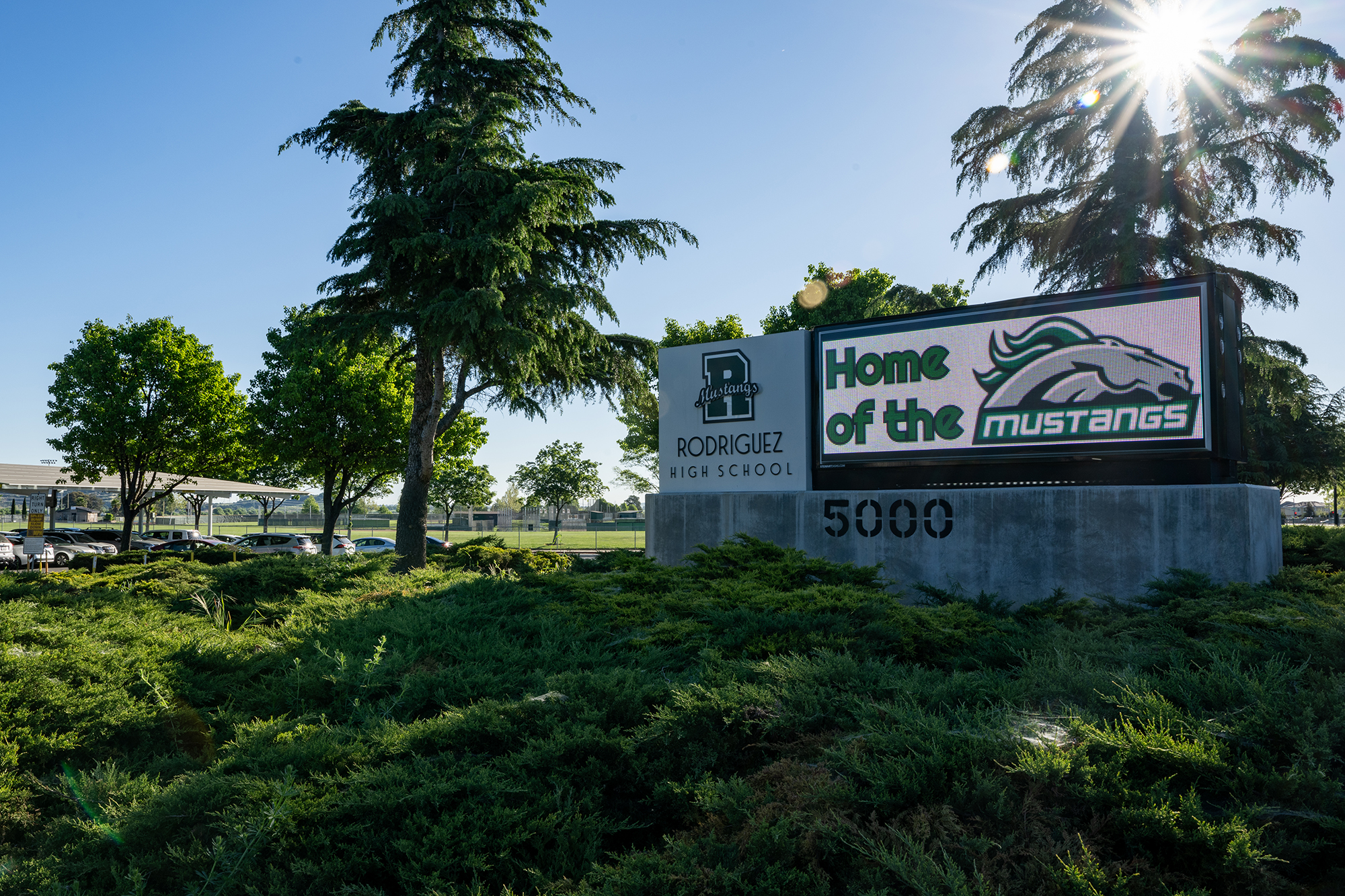 A sign that reads, &ldquo;Rodriguez High School&rdquo; and &ldquo;Home of the Mustangs&rdquo; outside surrounded by trees and bushes.