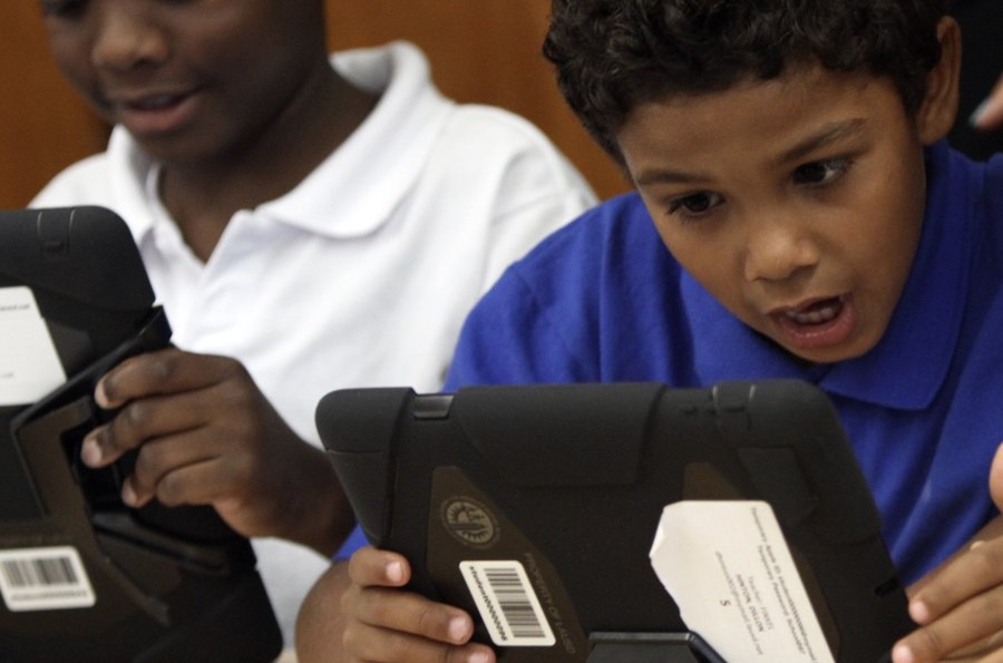Two young students looking at a tablet screen in a classroom.