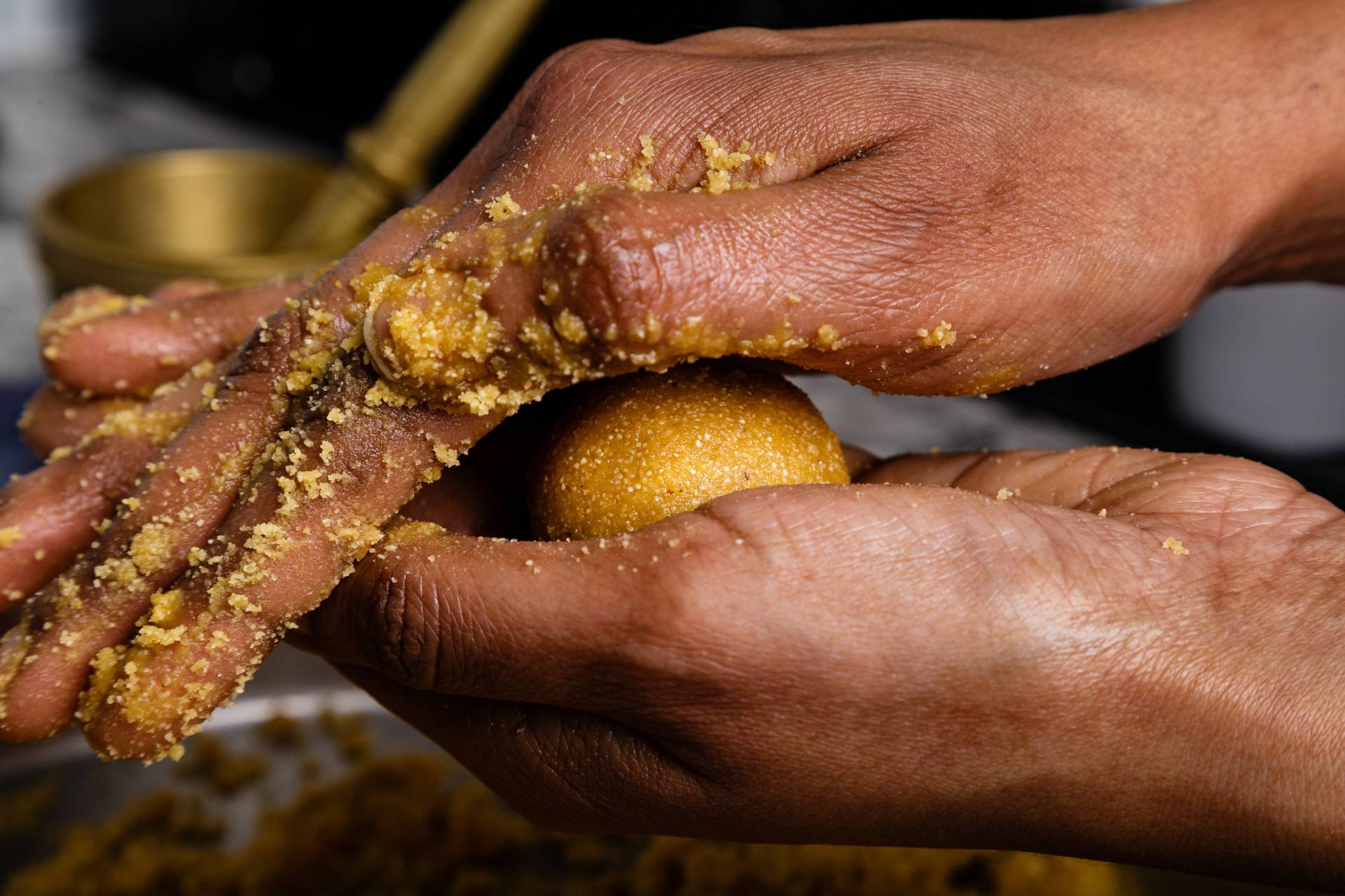 Hands squeezing golden-yellow dough into a ball shape to make besan ladoo.