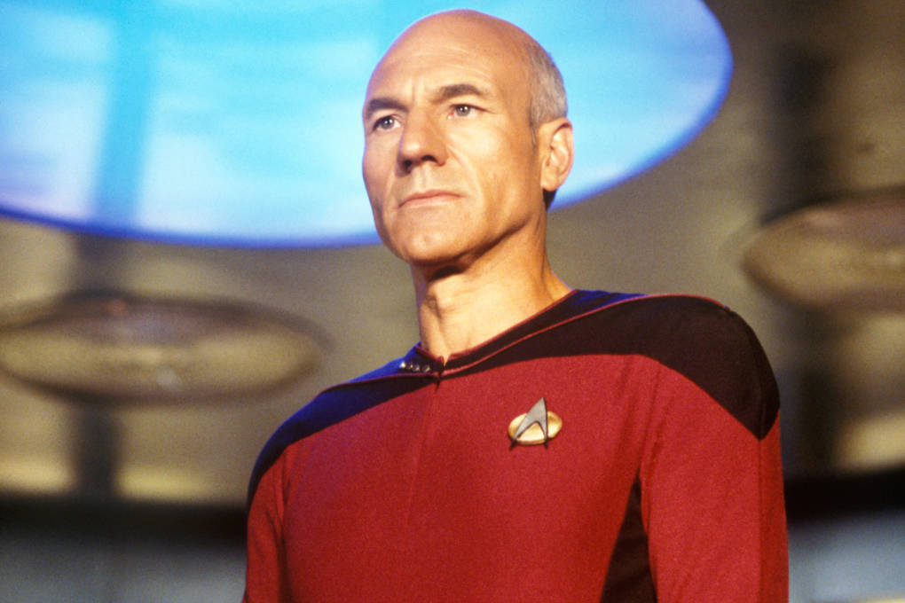 Patrick Stewart as Captain Jean-Luc Picard in red Starfleet uniform aboard the Enterprise