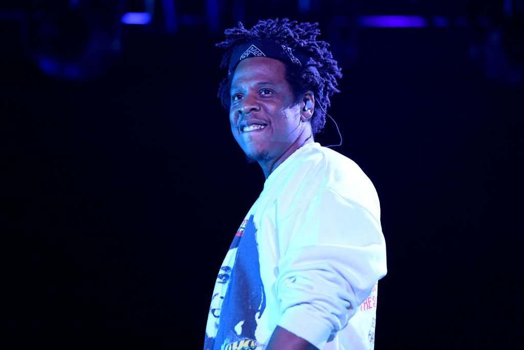 A Black man with short dreadlocks stands on stage under a blue light.