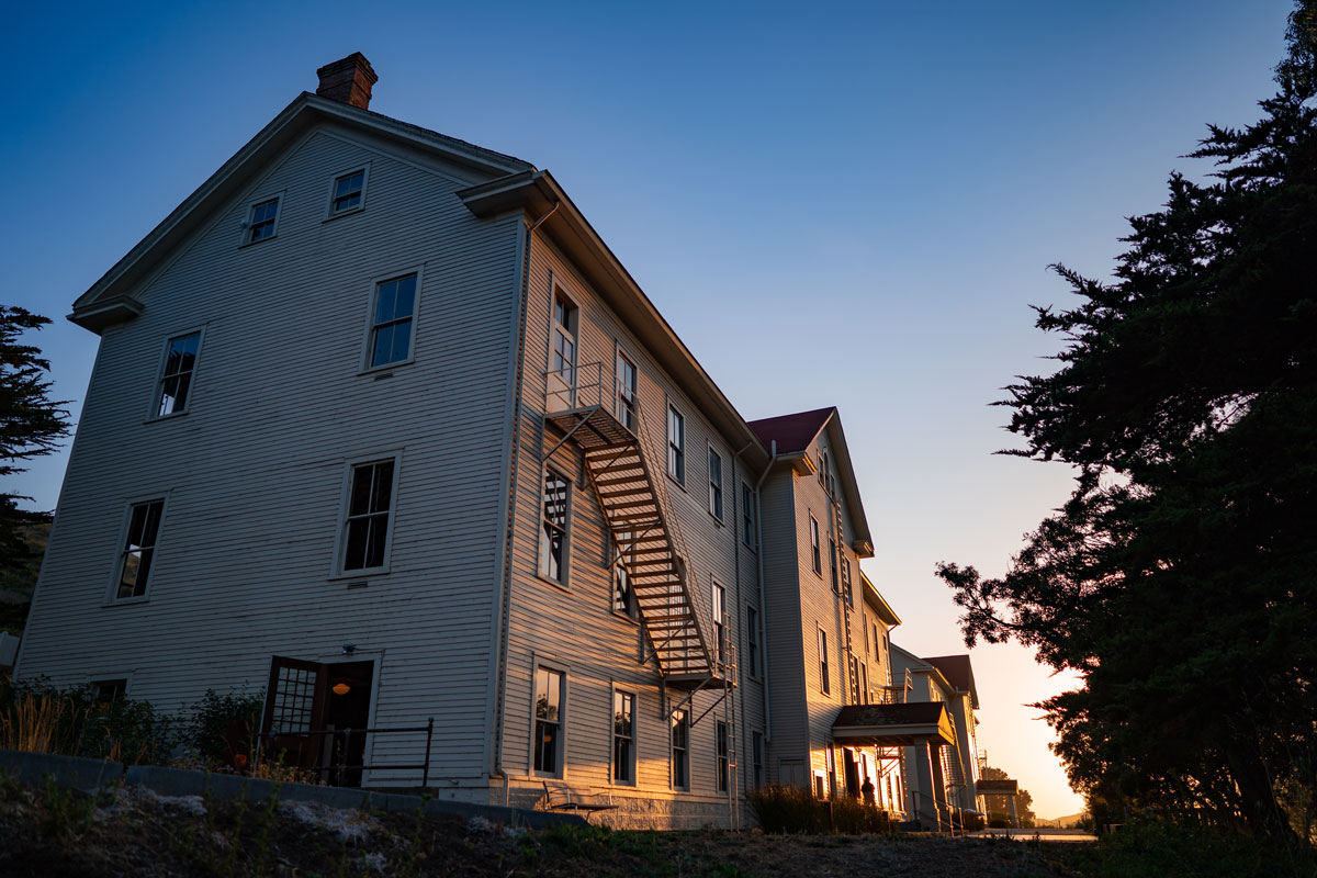 Two former army barracks seen at dusk with blue and orange light