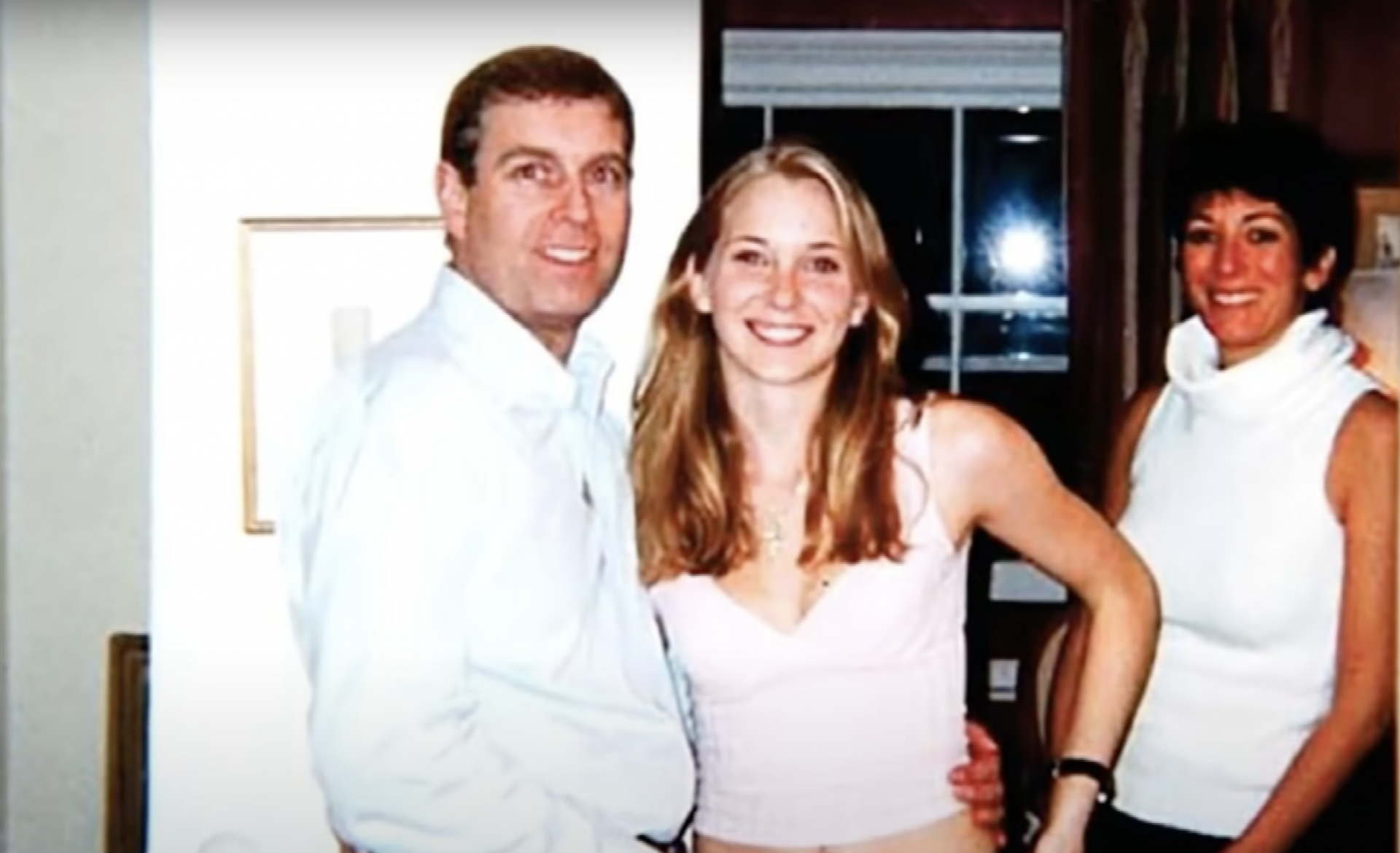A middle aged white man wearing a white shirt rests his hand on the waist of a slender white young woman with long blonde hair. She is wearing a tight pink tank top.
