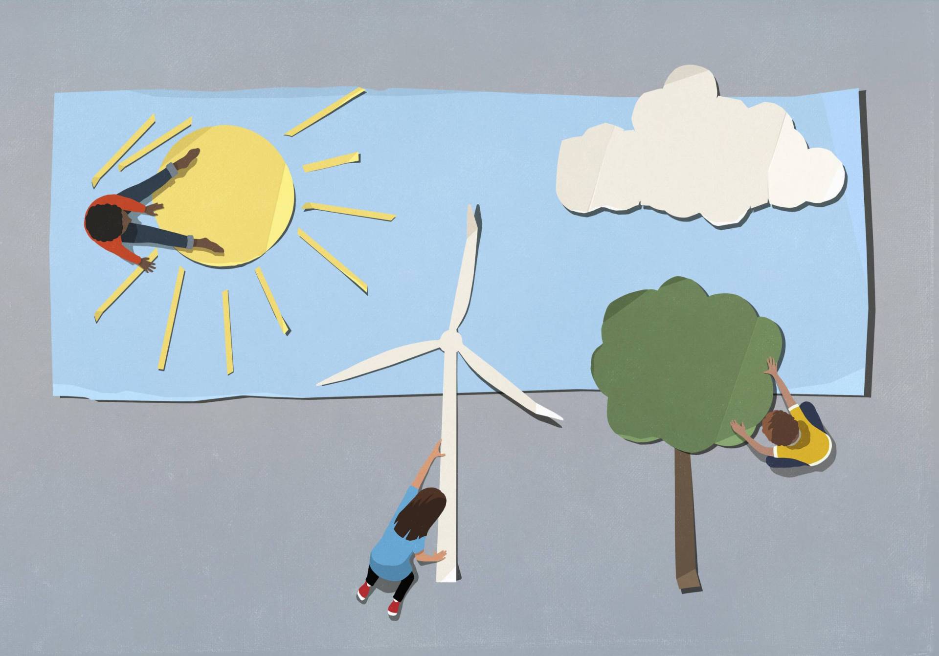 Paper collage of children working on laying out paper cutouts of a windmill for wind energy, a tree, and a sun, seen from above.