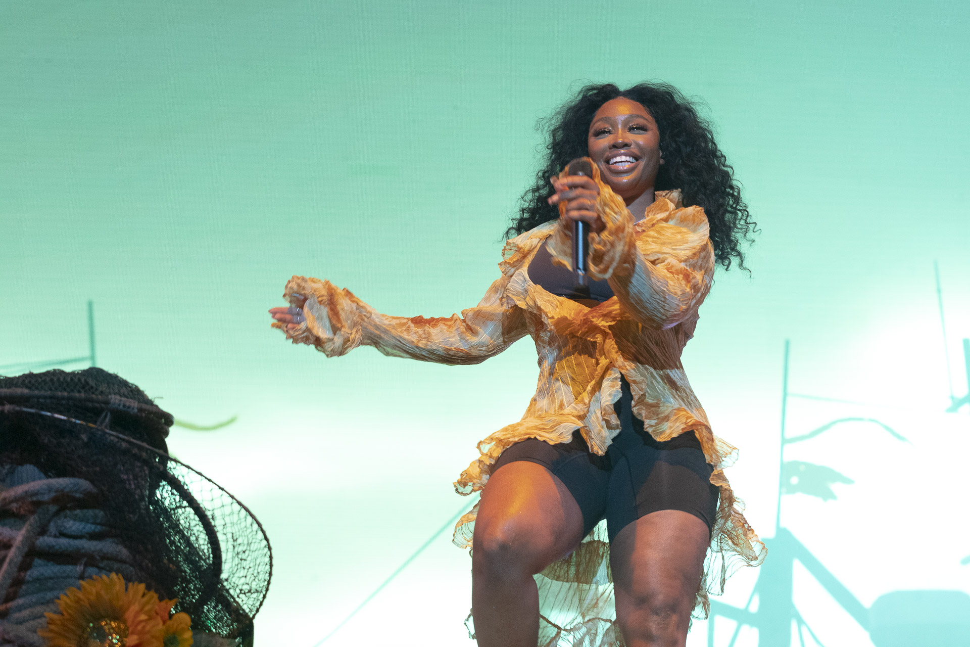 A Black woman stands behind a microphone stand on stage. She is dancing and smiling.