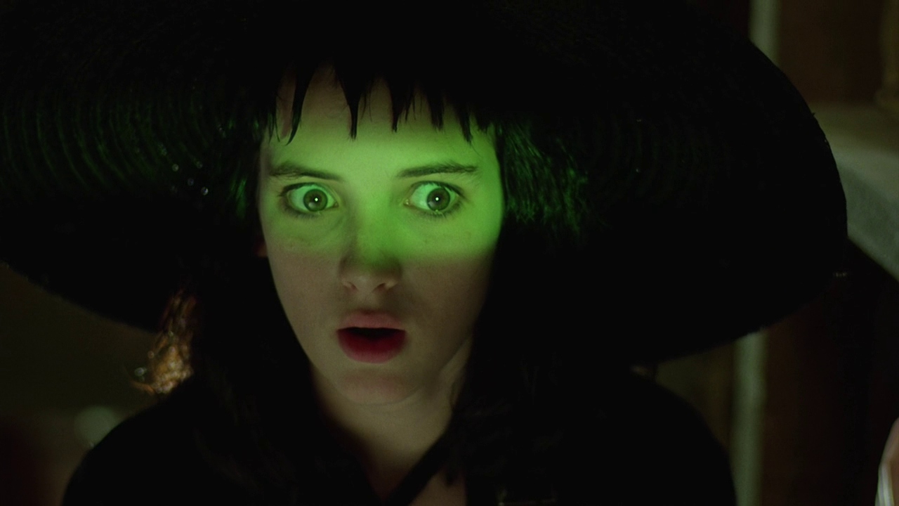 A teenage girl, green light glowing across her eyes, looks at something off in the distance with great horror.