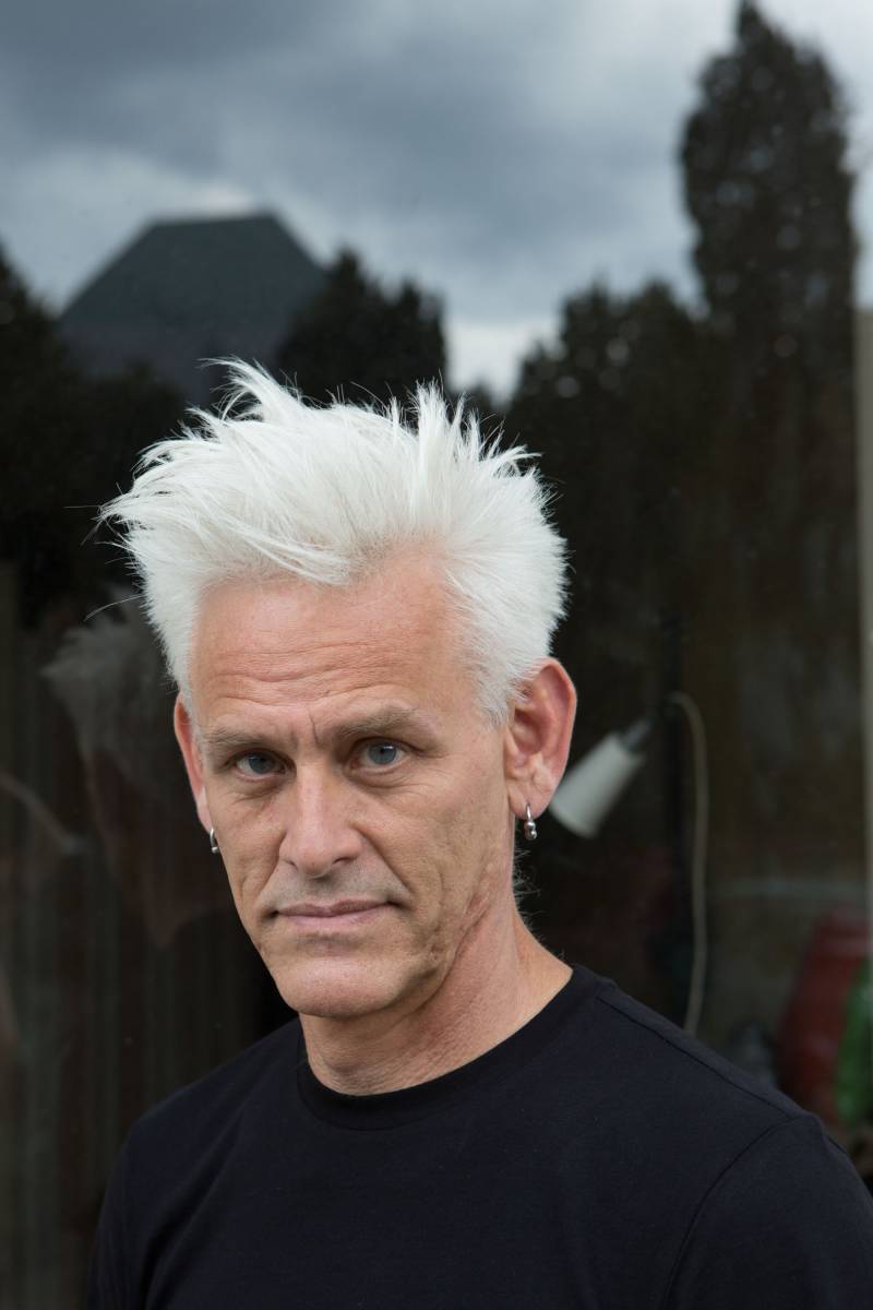 Jess Curtis, a white man with short white hair and a black T-shirt, looks into the camera.