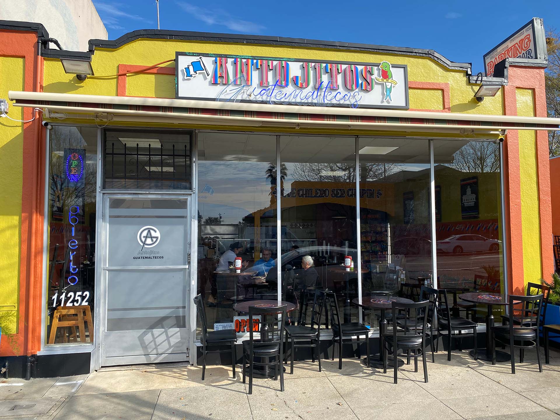 Exterior of the Antojitos Guatemaltecos restaurant with a yellow facade and a handful of outdoor tables on the sidewalk.