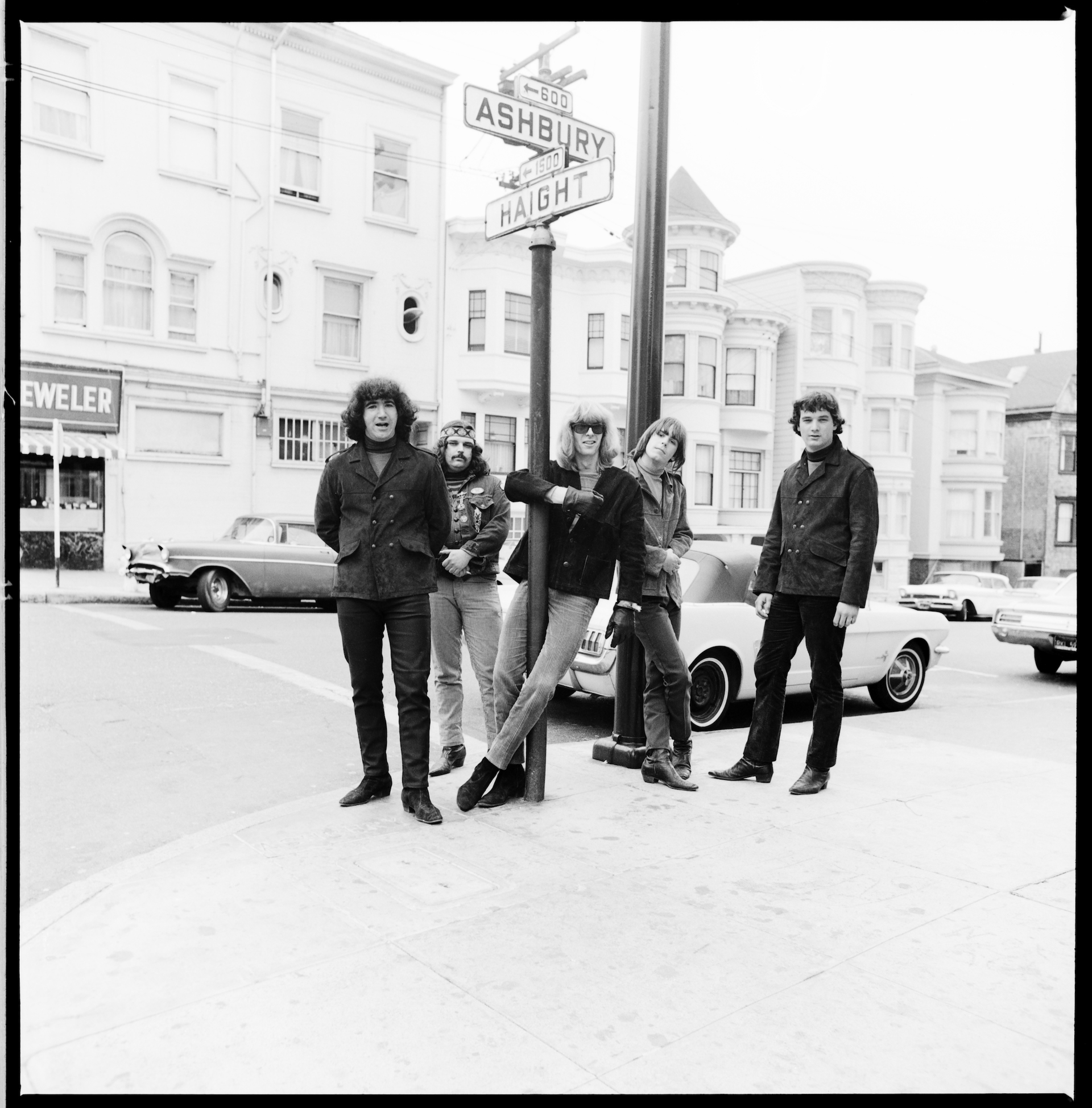 Five young men with long hair gather around and pose next to a street sign at an intersection that reads Haight Ashbury.