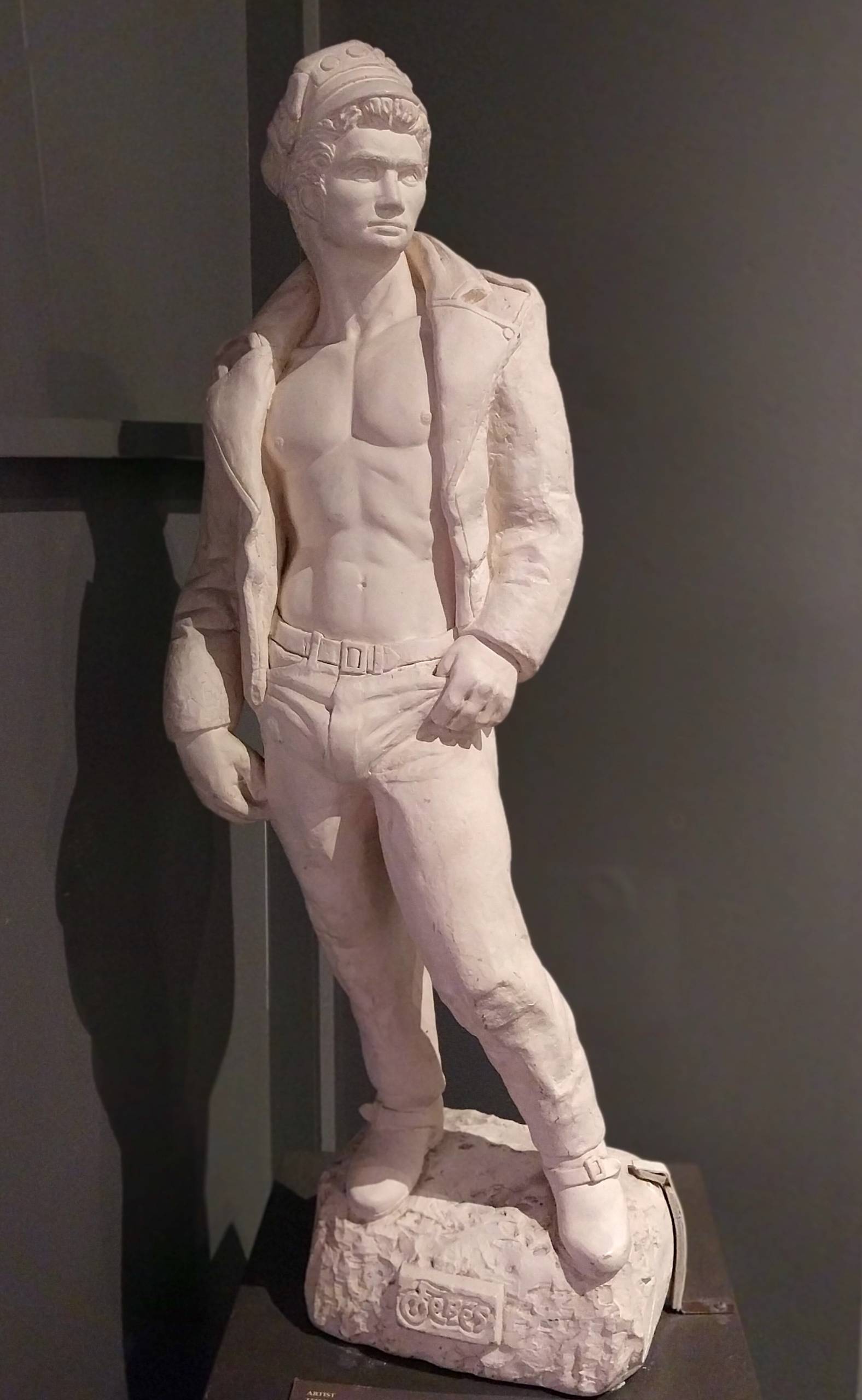 A white marble statue depicting a shirtless biker, with his hand hooked in one pocket.