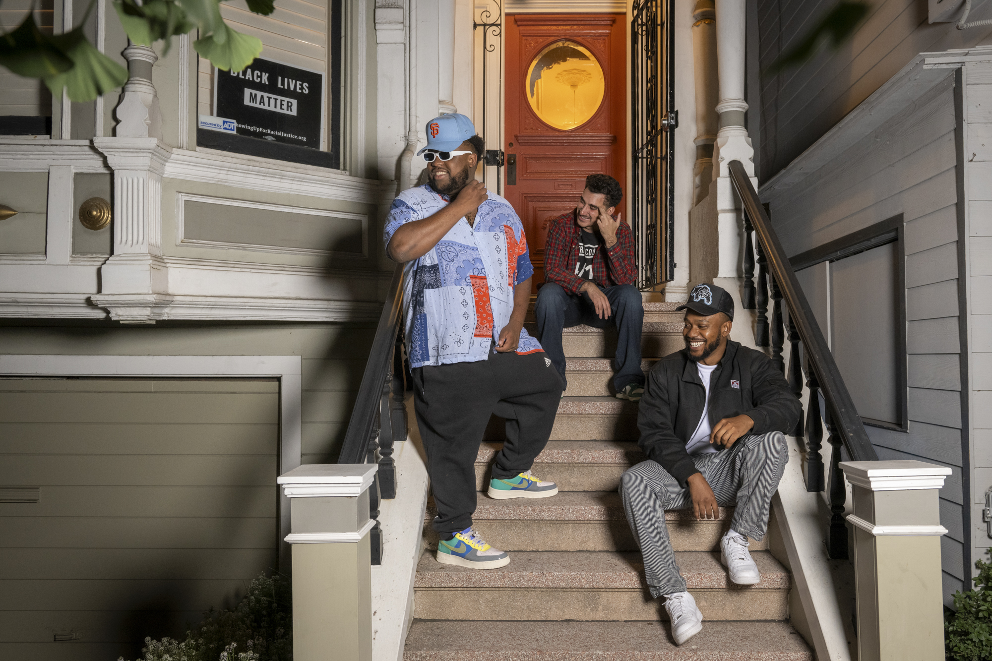 Three people sit and lean on the steps outside of a home and smile.