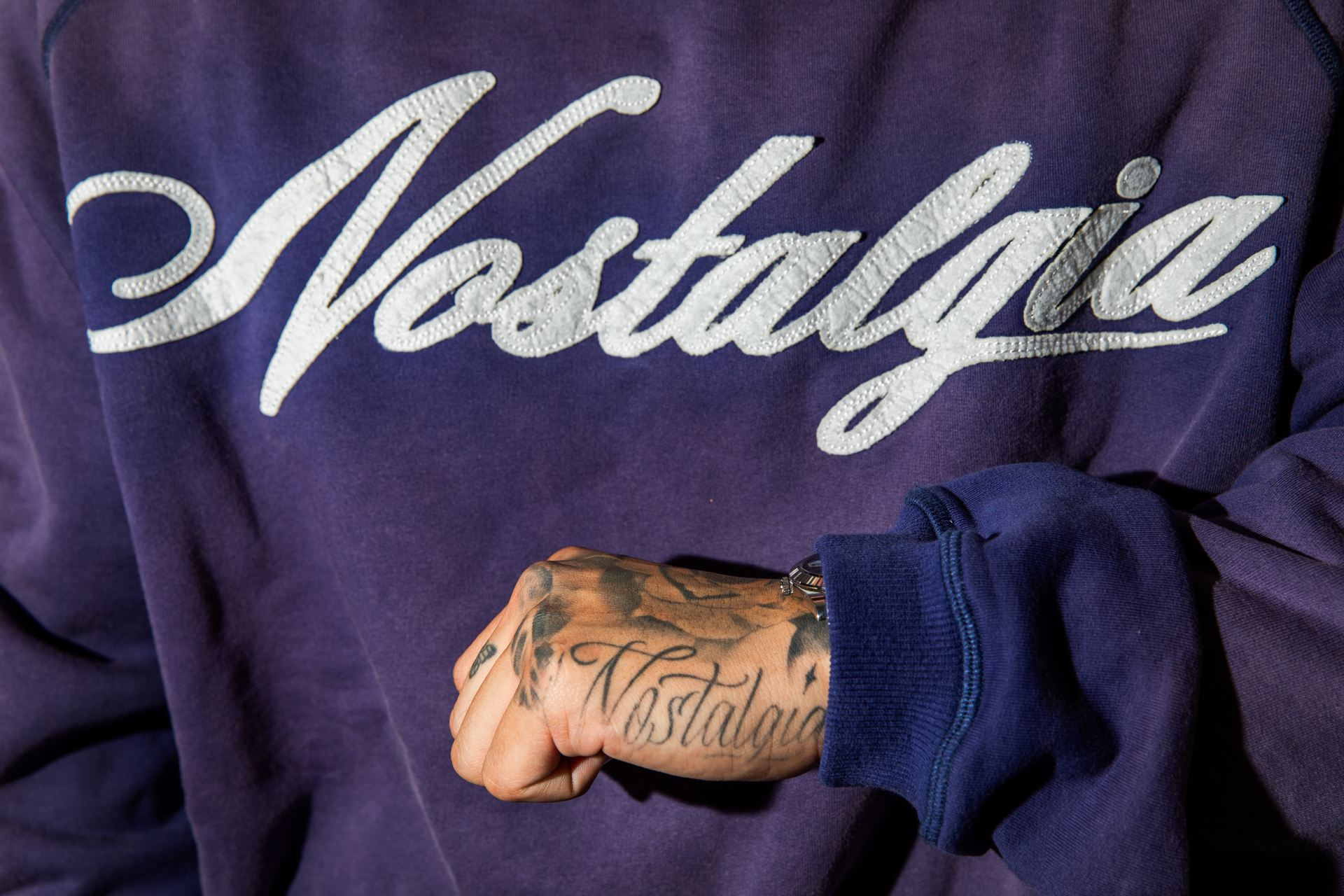 A purple sweatshirt with white lettering fills the photo frame. A hand is held in front.