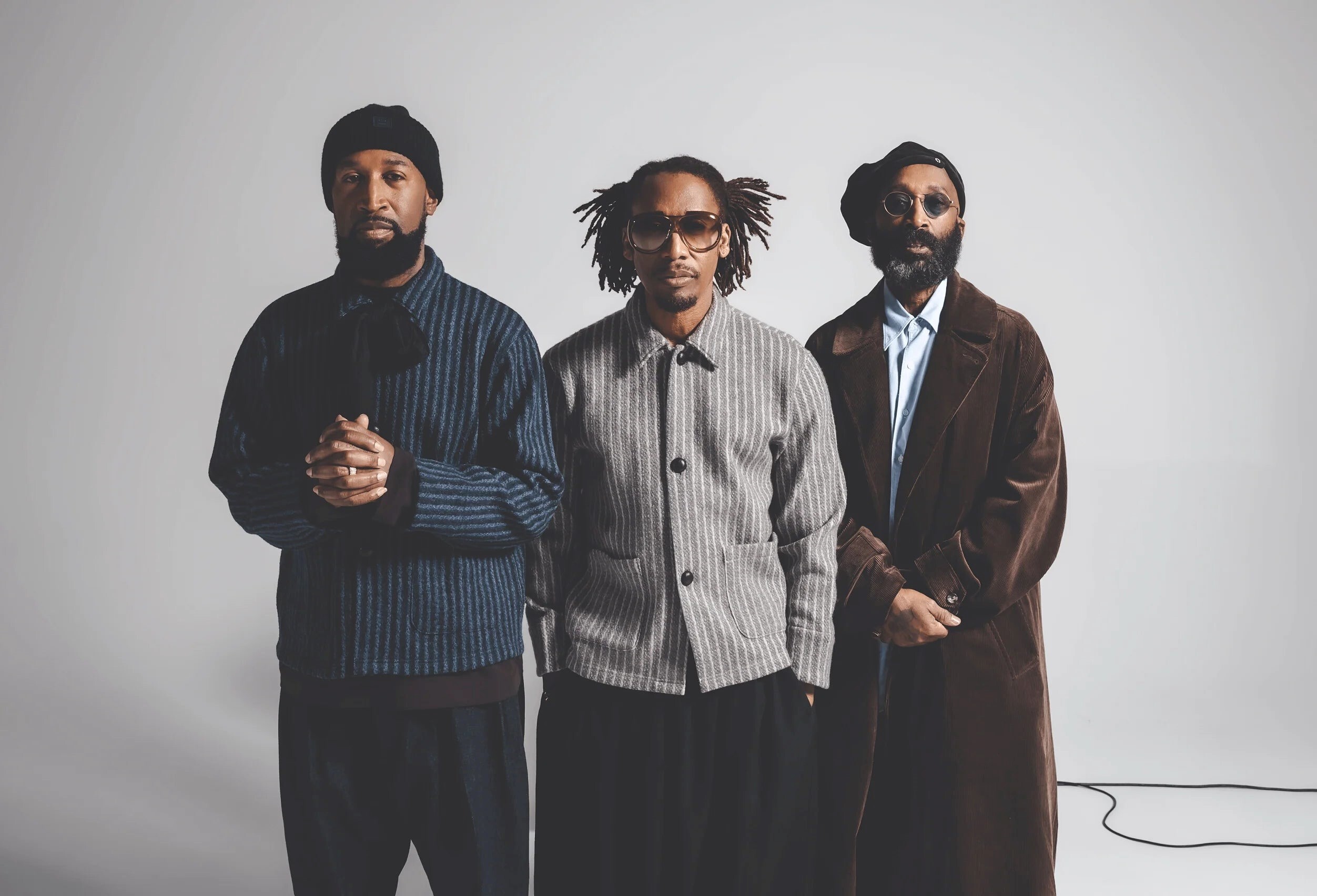 Three Black men in semi-formal fashionable clothes stand in a row, looking into the camera