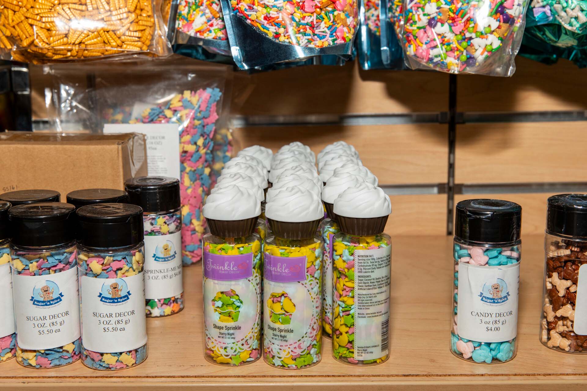 A shelf displaying a variety of colorful sprinkles in small jars and large plastic bags.