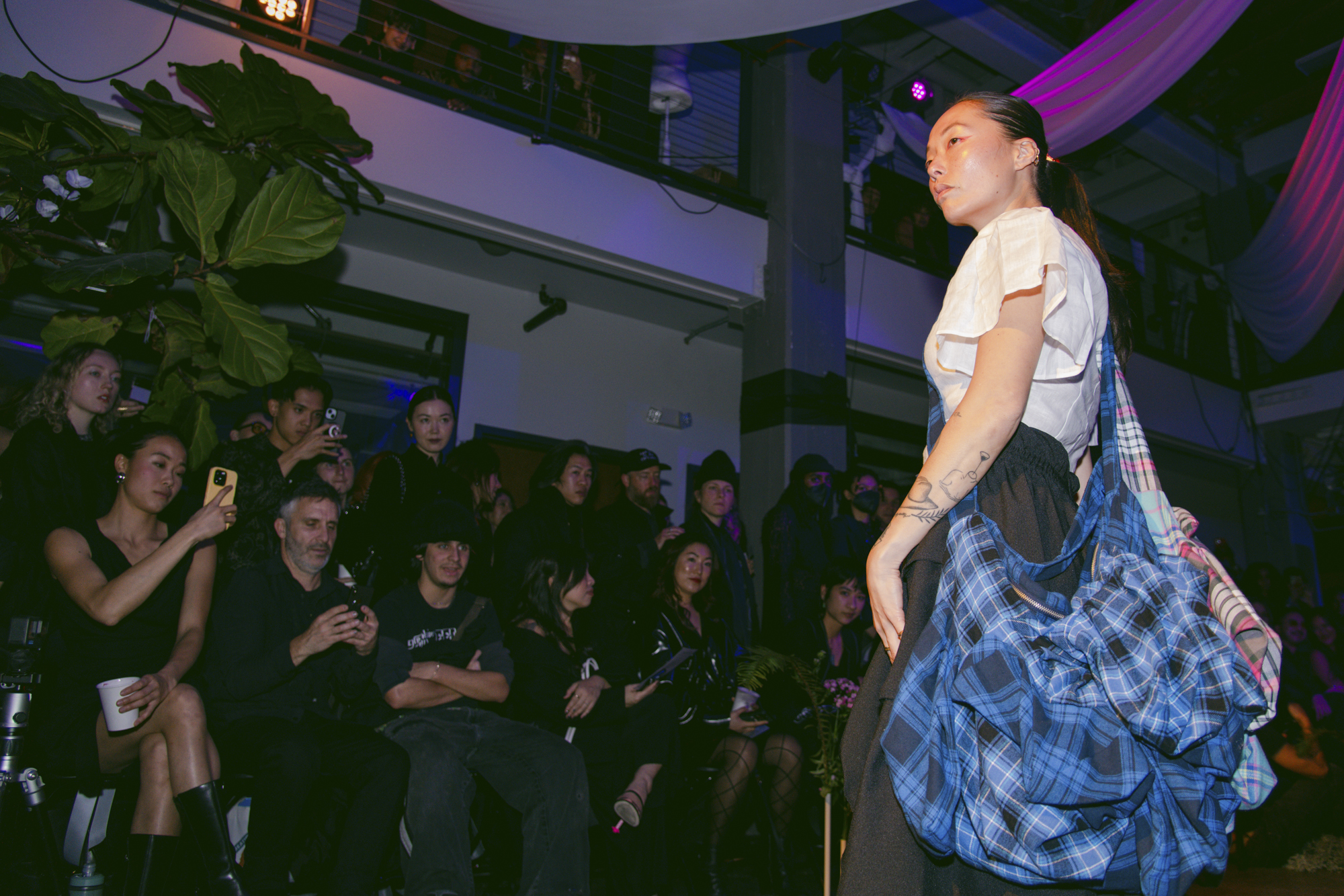 A model wearing a large bag stands in front of a large group of people.