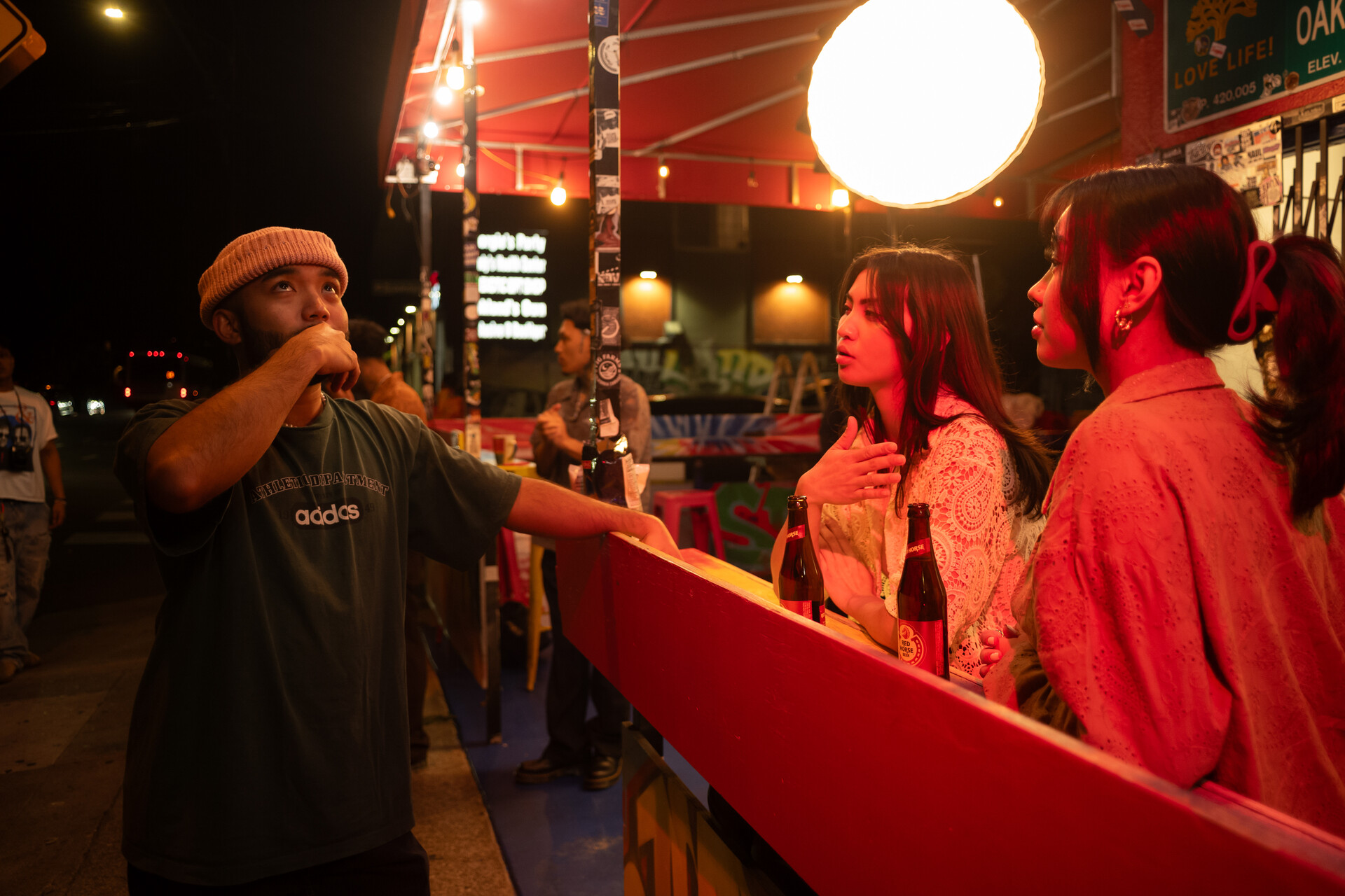 A videographer speaks to models between shots at a dimly lit Filipino restaurant.