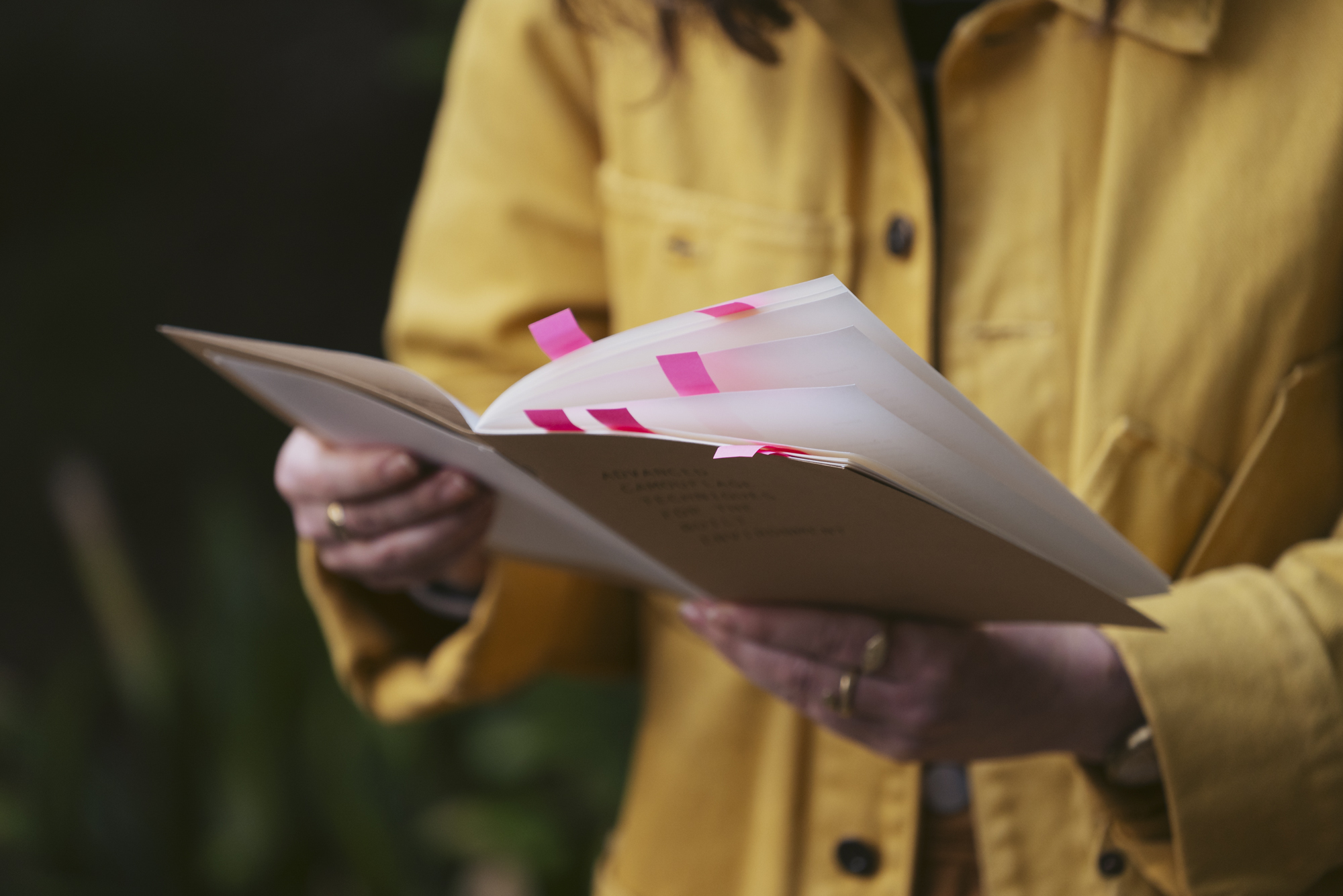 A person holds a thin book marked with pink tabs.