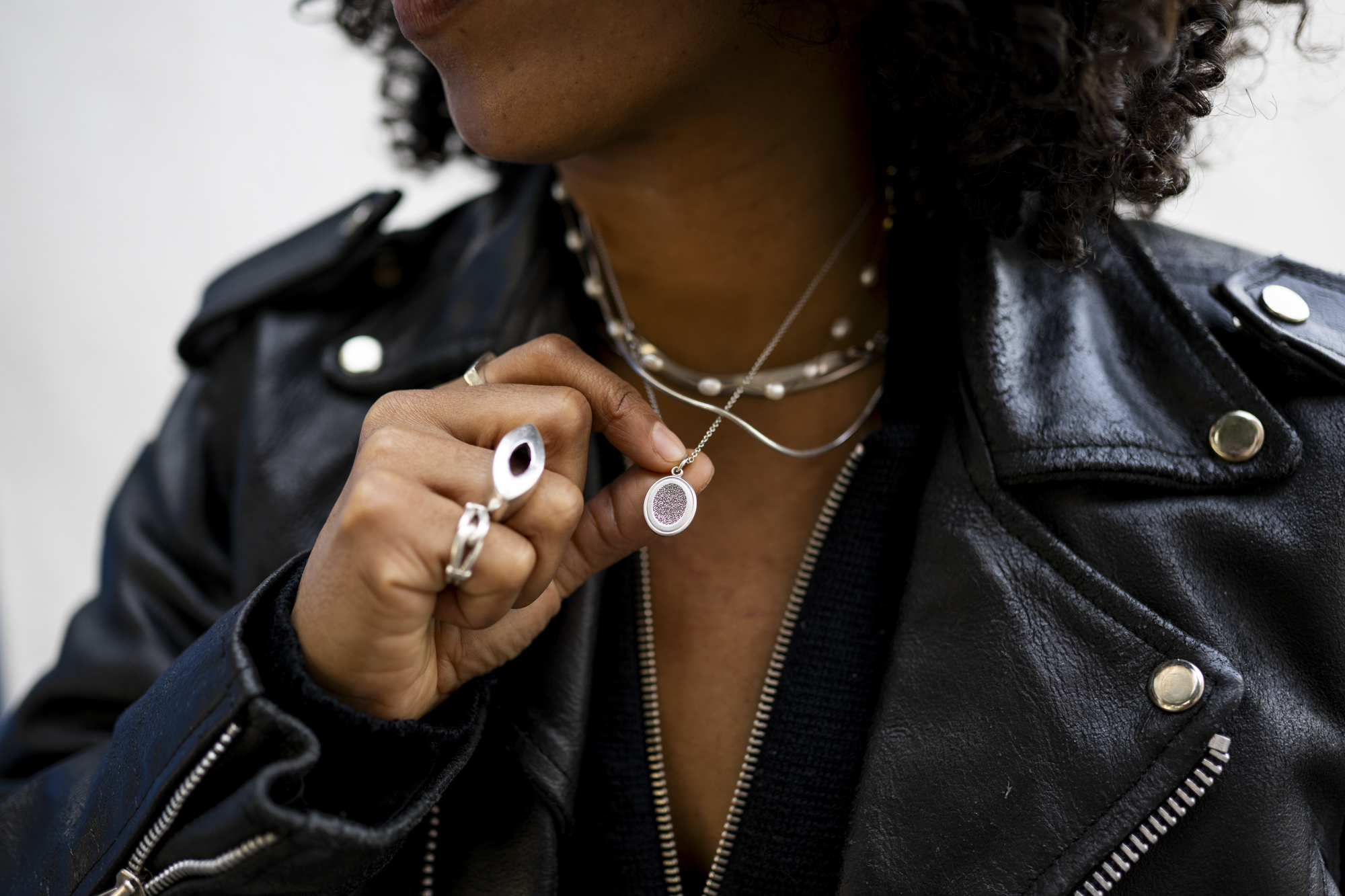 A person with a leather jacket holds a circular necklace.