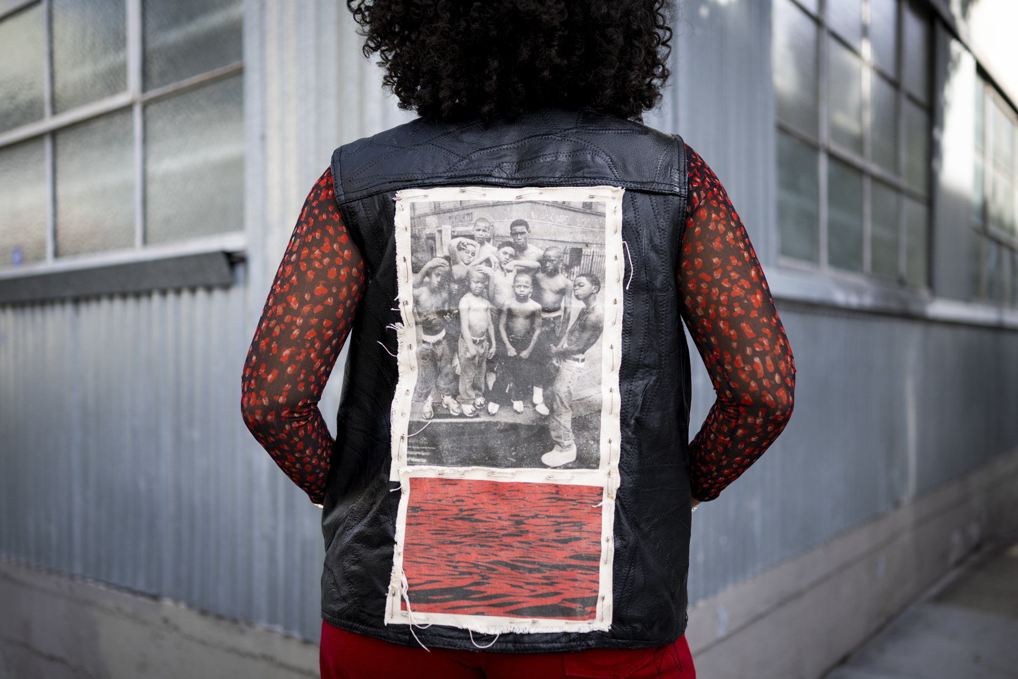 A person long hair poses for a photo with an old photo stitched to the back of their leather vest.